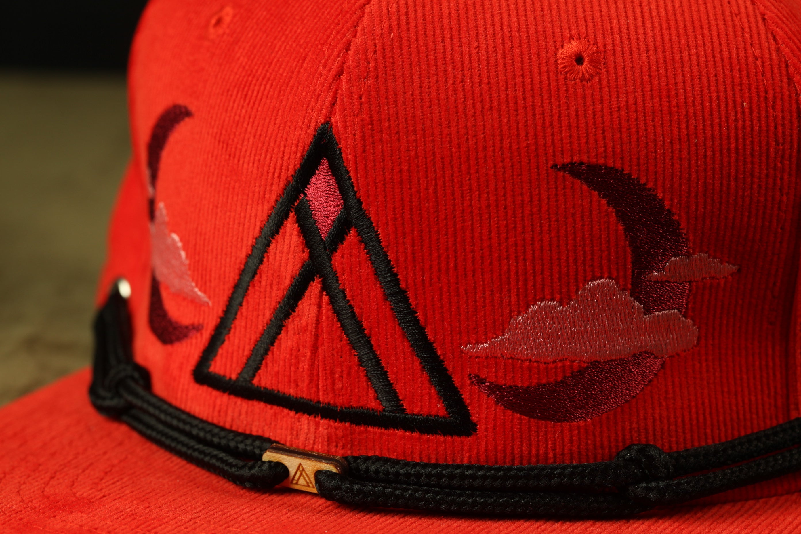 A close-up view of a red baseball cap with a black brim and a black and red triangle design on the front.