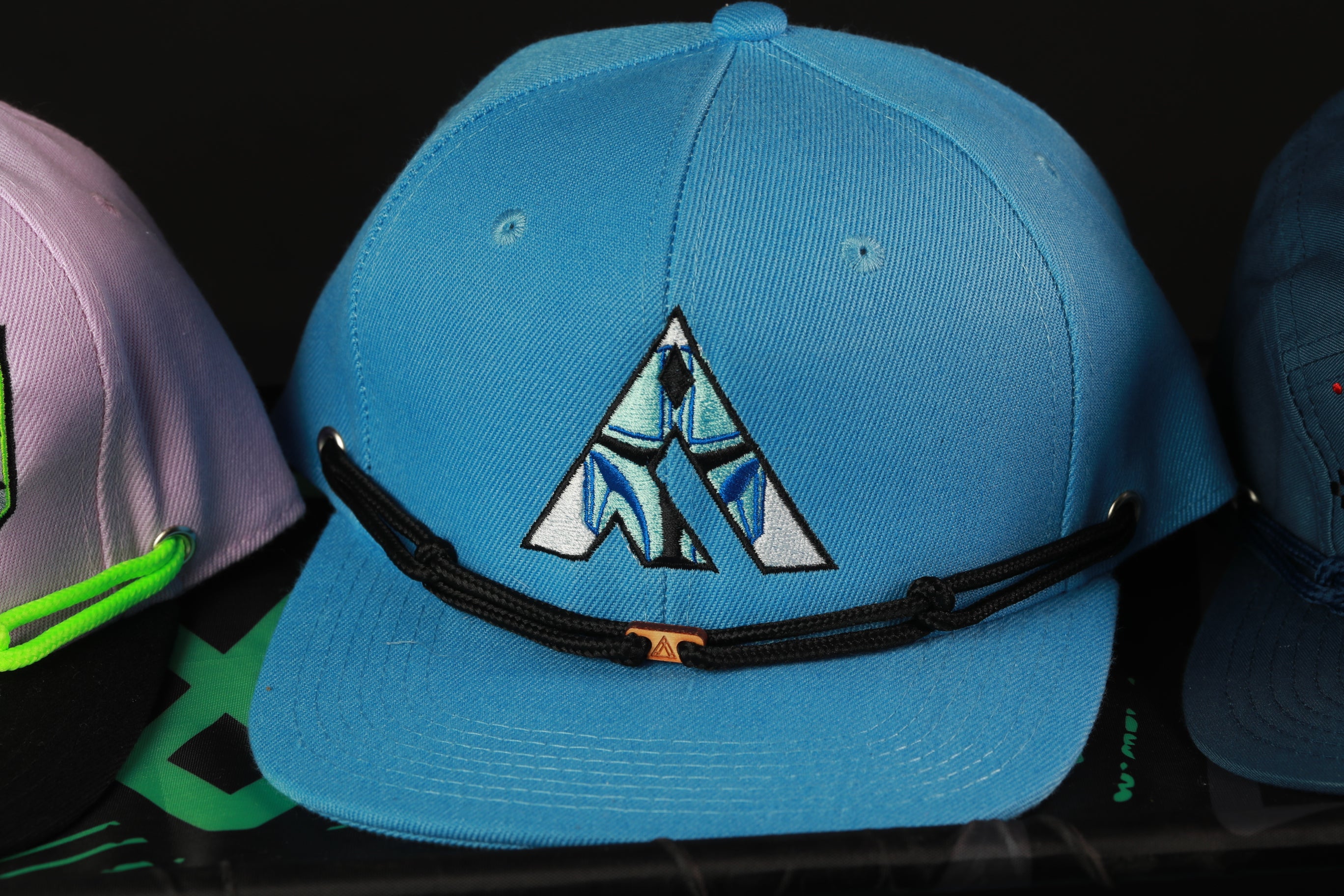 A close-up view of a blue baseball cap with a unique logo, displayed among other hats.