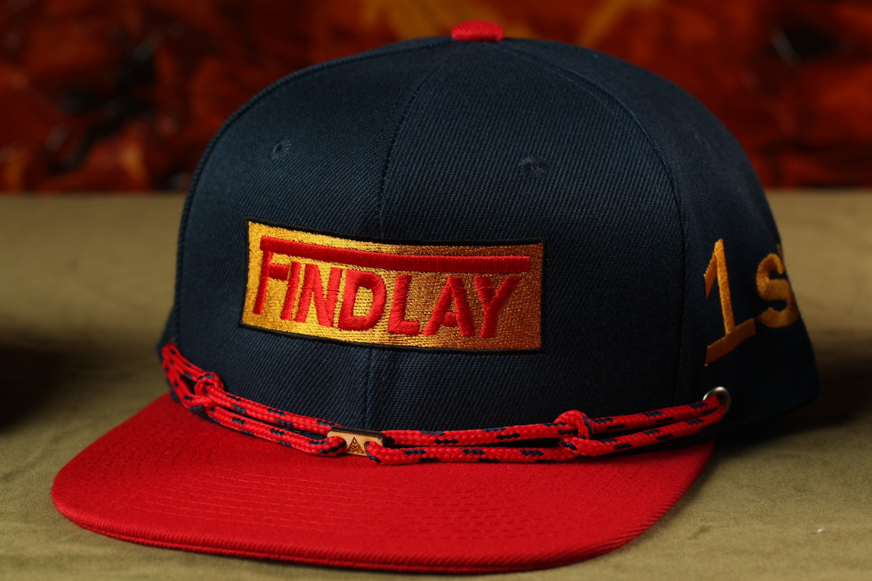 A navy blue baseball cap with a red brim and a red and gold embroidered logo on the front.