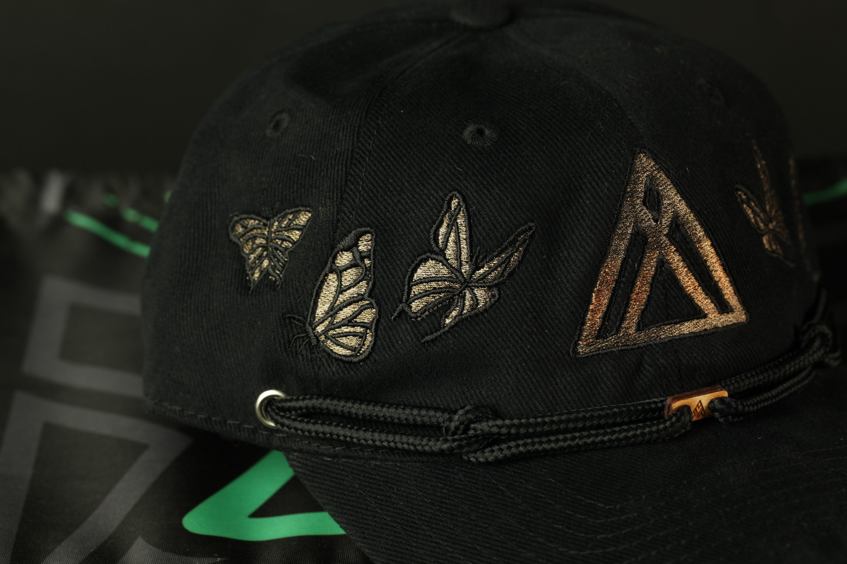 A close-up view of a black baseball cap with gold butterfly and triangle designs on the front.