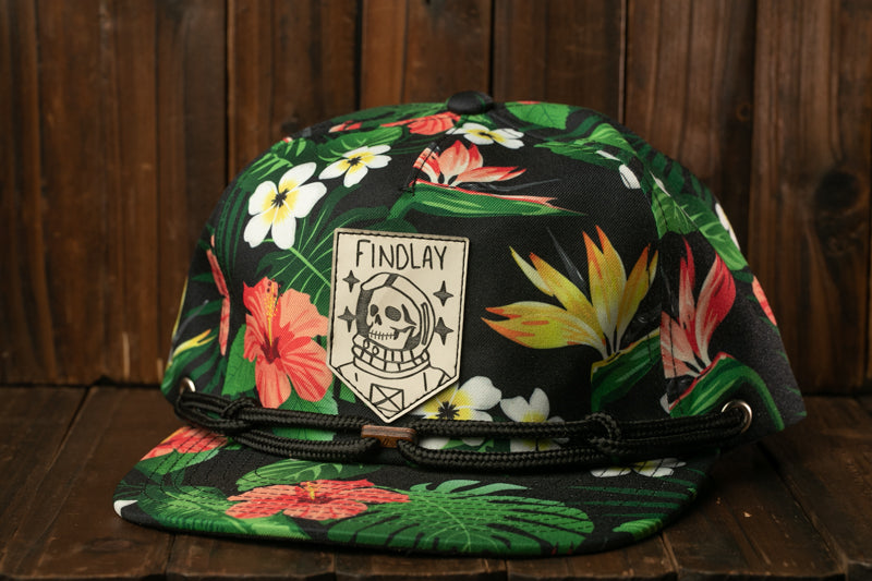 A colorful floral cap with a skull design and the text "FINDLAY" printed on it, placed on a wooden surface.
