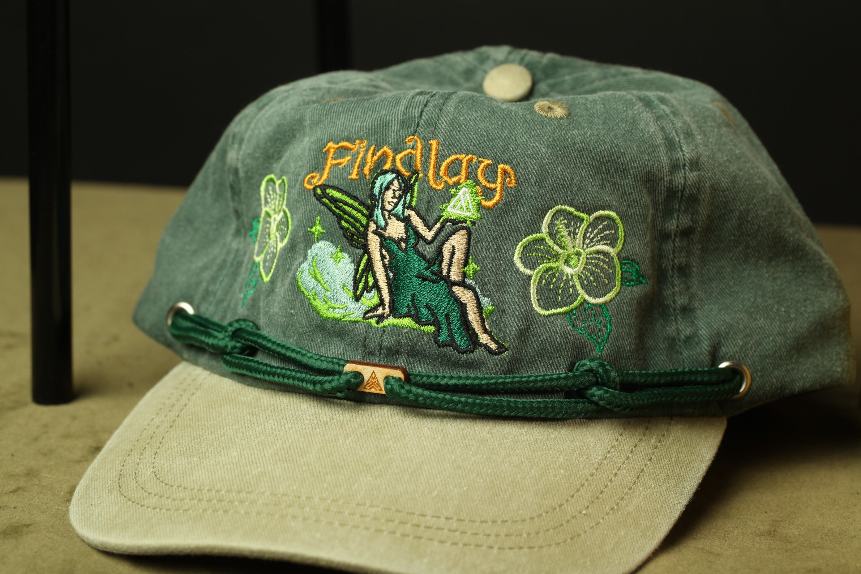 A green baseball cap with a woman's figure and floral designs on it.