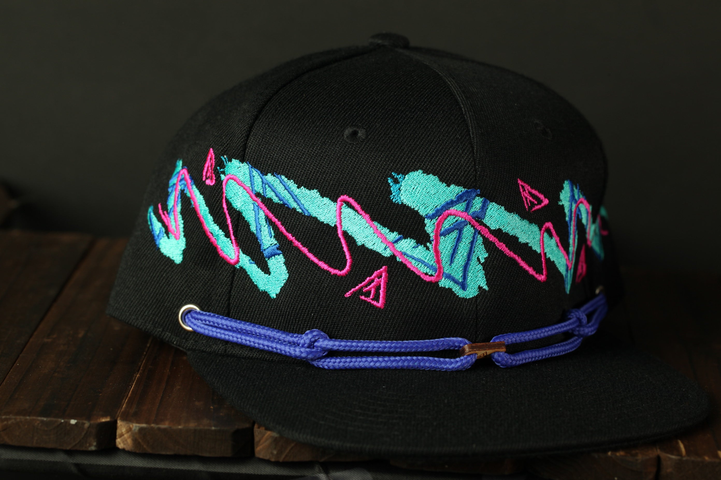 A black baseball cap with a colorful, abstract design on the front, including pink and blue lines and shapes.