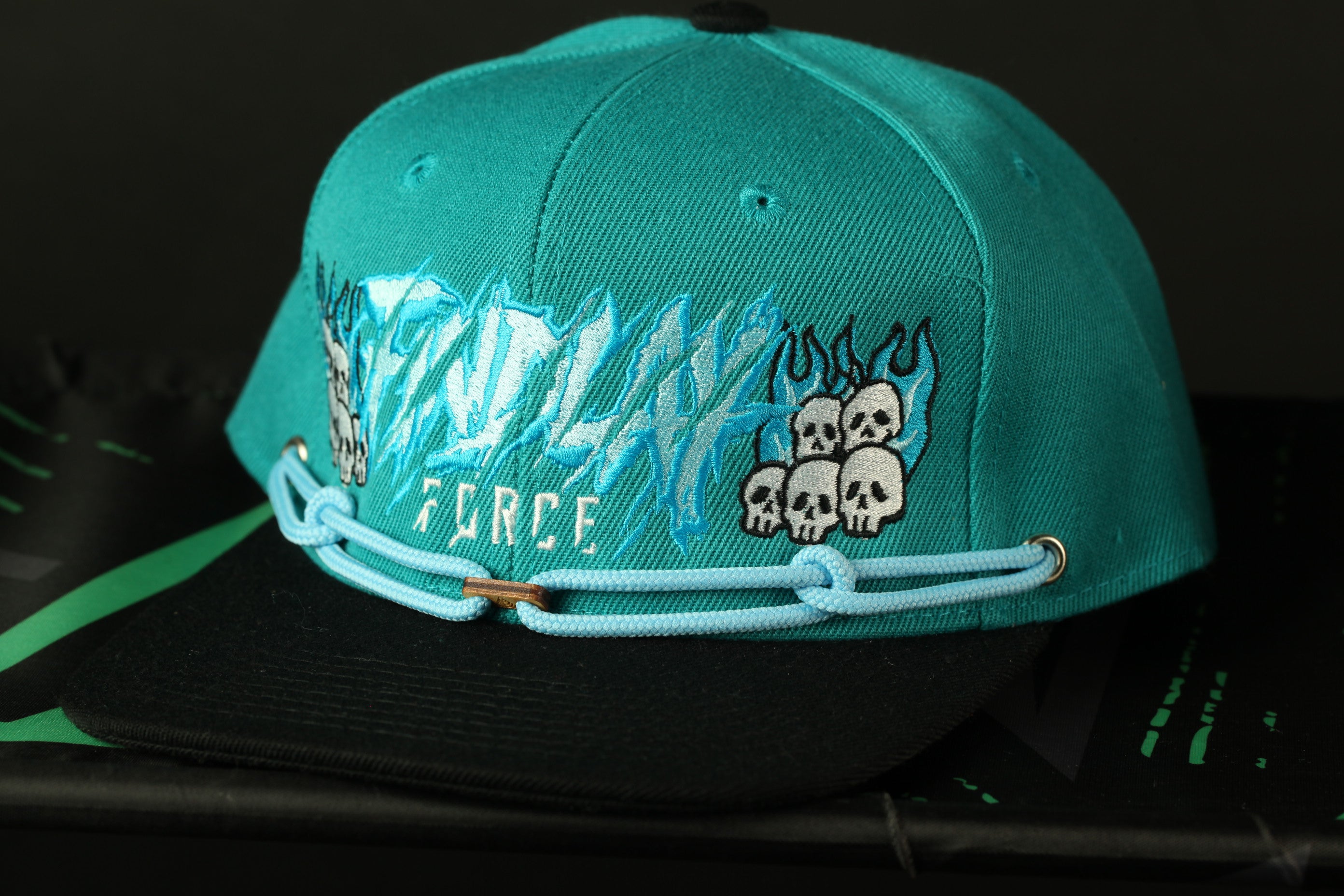 A turquoise baseball cap with a graphic design featuring skulls and flames on the front.