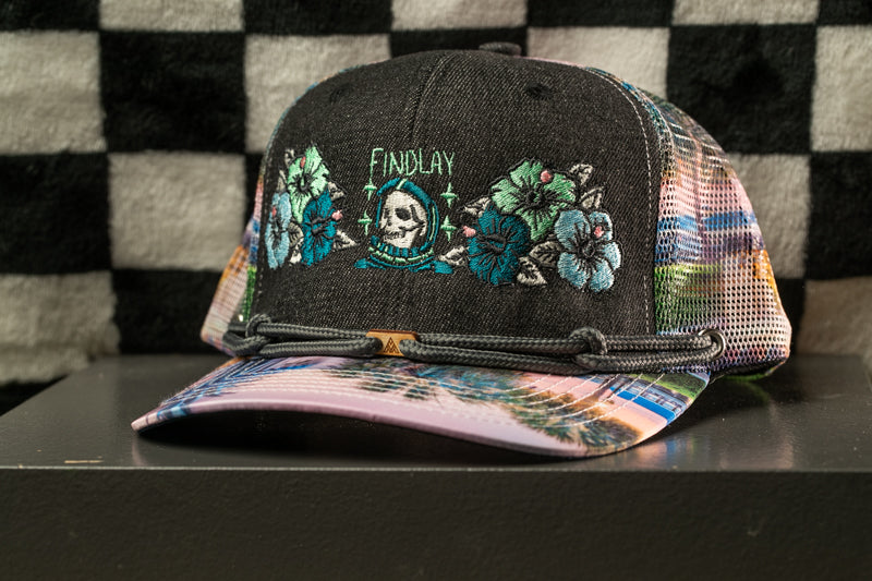 A black baseball cap with colorful floral embroidery and a skull design, displayed on a black surface against a checkered background.
