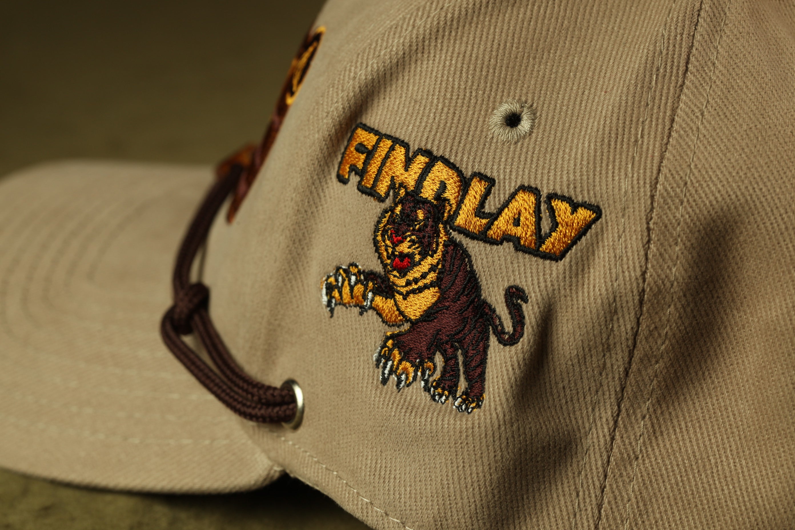A close-up view of a beige baseball cap with a tiger embroidered on it.