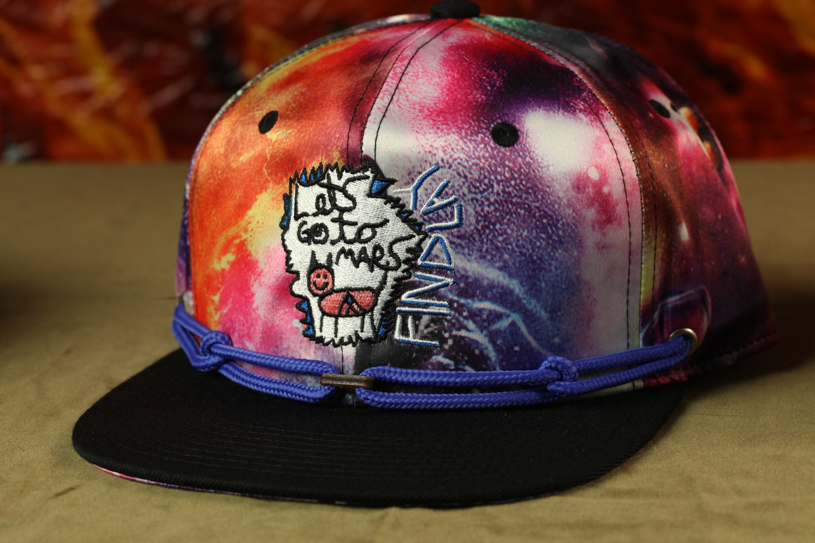 A colorful, tie-dye baseball cap with a peace sign and a skull design, featuring a blue band around the brim.