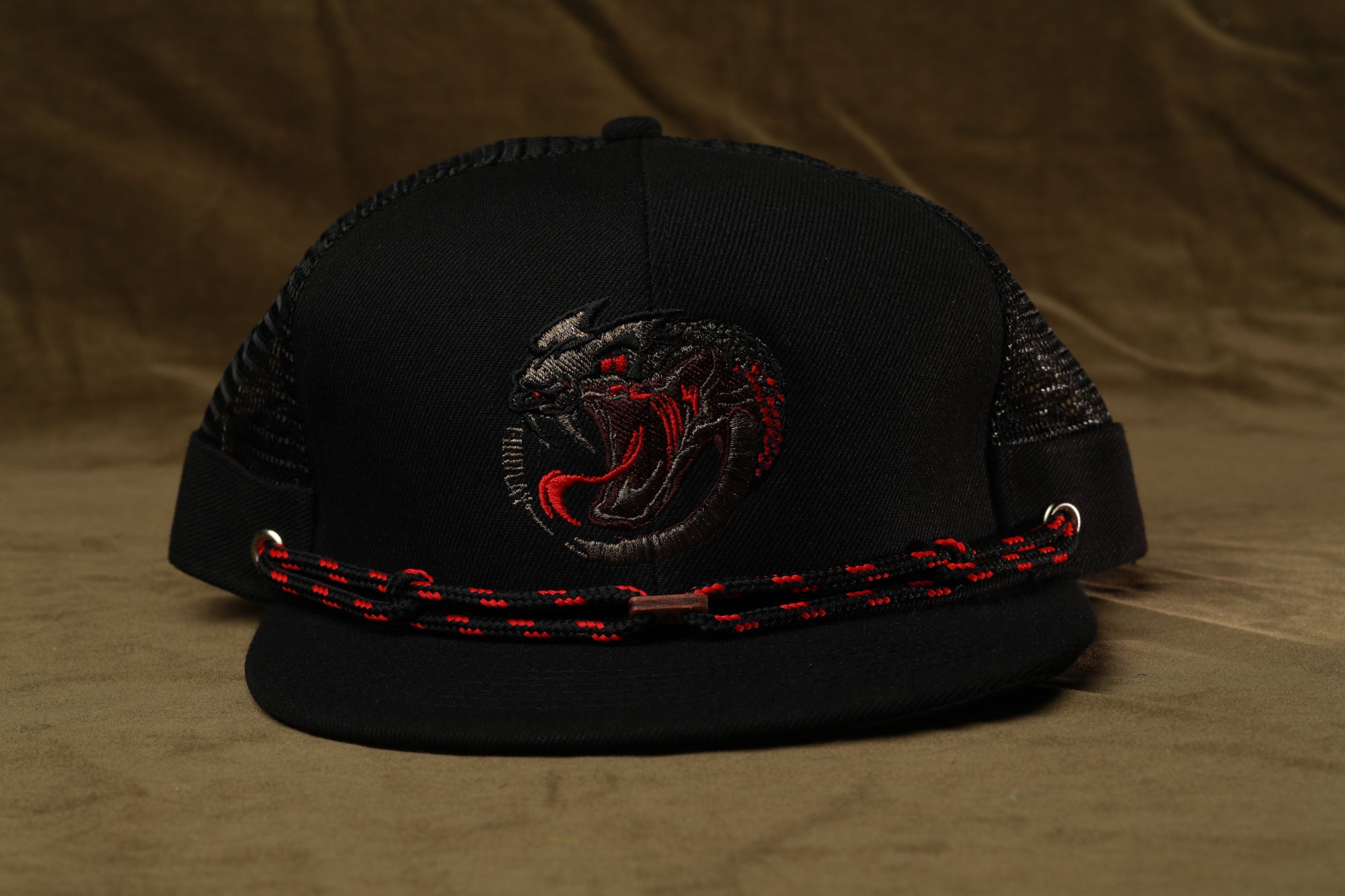 A black baseball cap with a red and black snake design on the front, and a red and black chain strap around the brim.