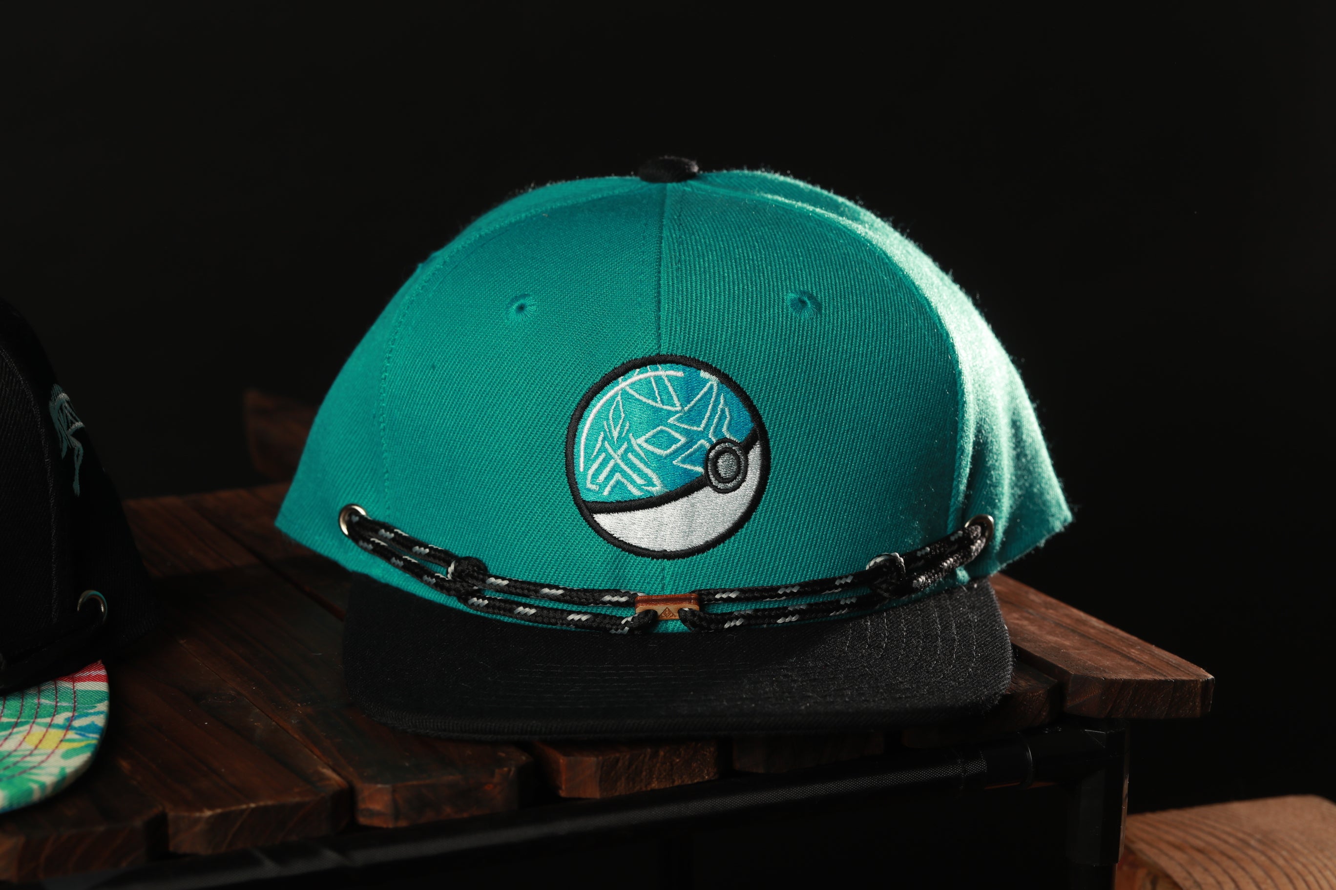 A turquoise baseball cap with a Pokemon-inspired design sits on a wooden surface.