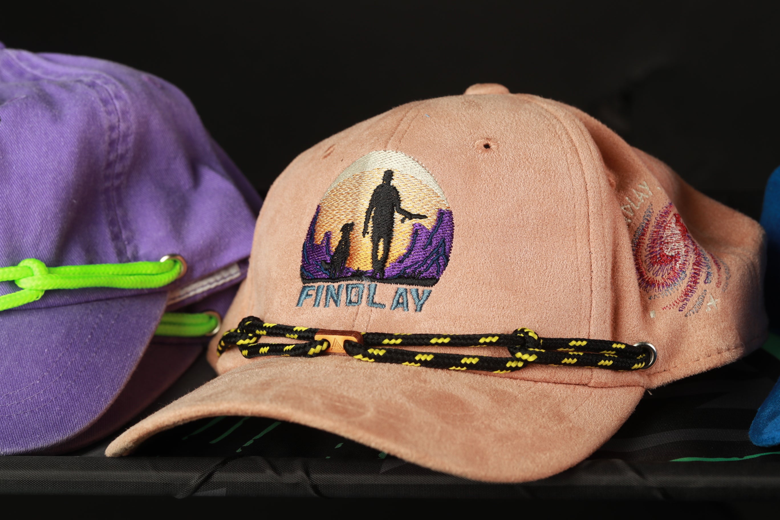 a close-up of a pink baseball cap with a graphic design and a black and yellow string.
