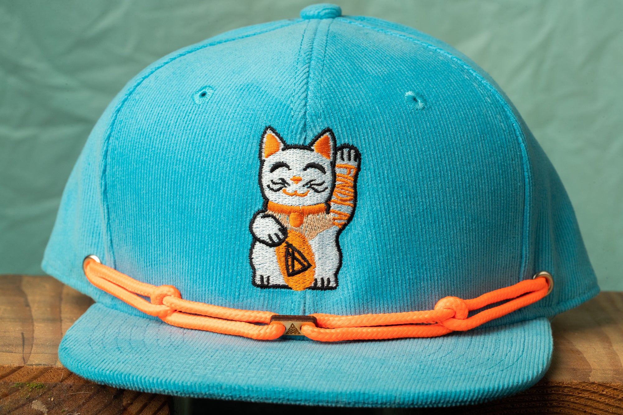 A turquoise baseball cap with an embroidered cat design on the front.
