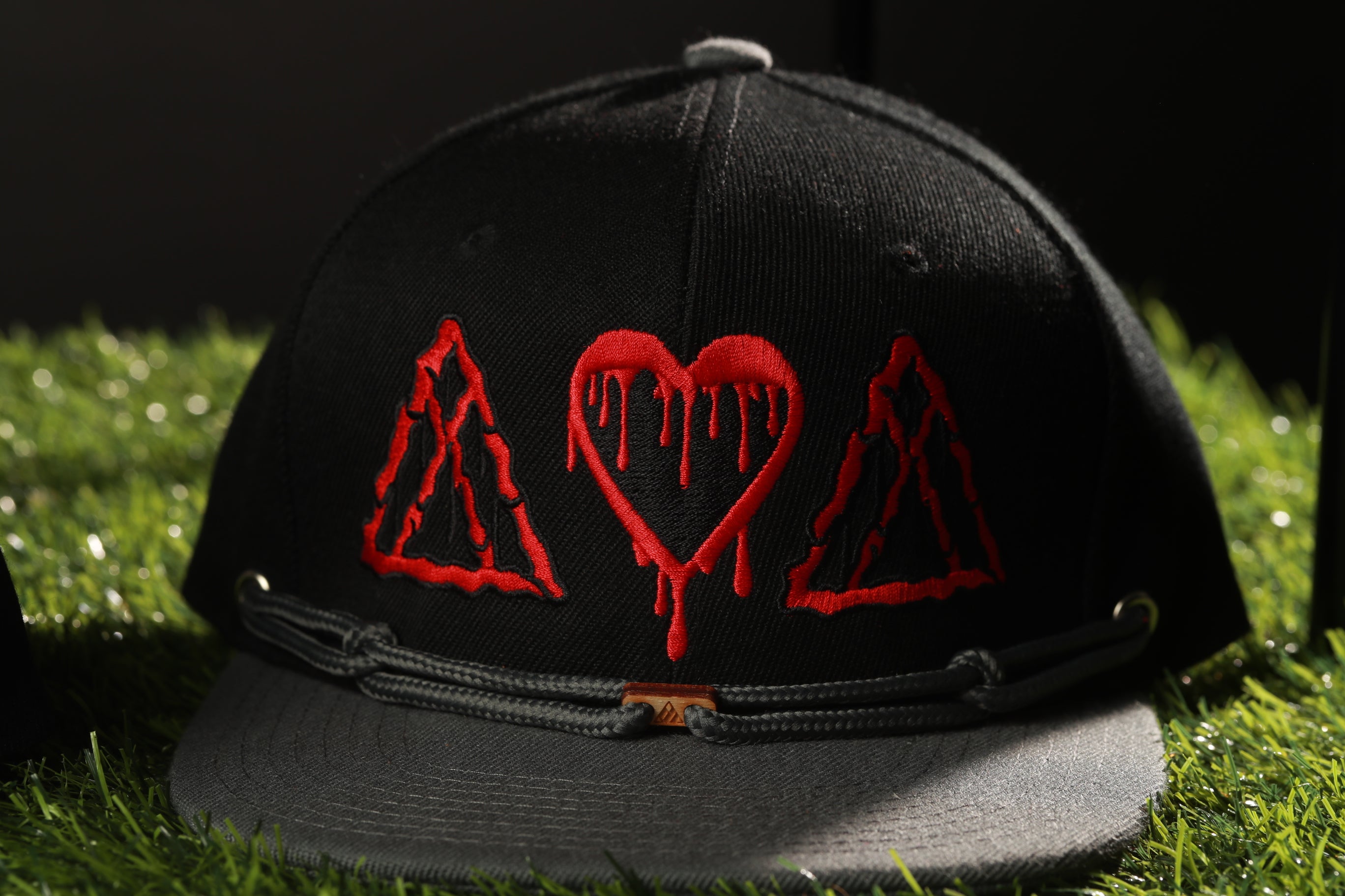 A black baseball cap with red heart and triangle designs on it, placed on a grassy surface.