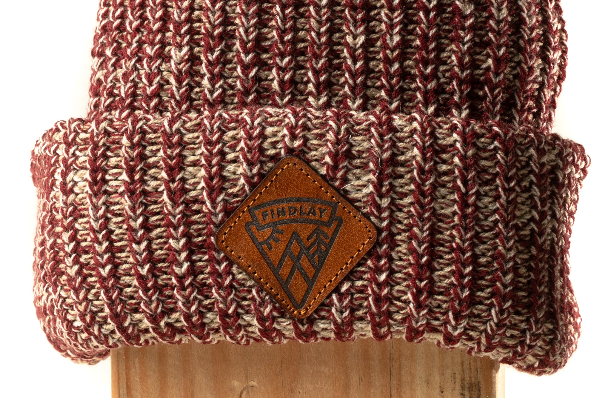 A close-up image of a knitted beanie with a leather patch on the front, featuring a logo.