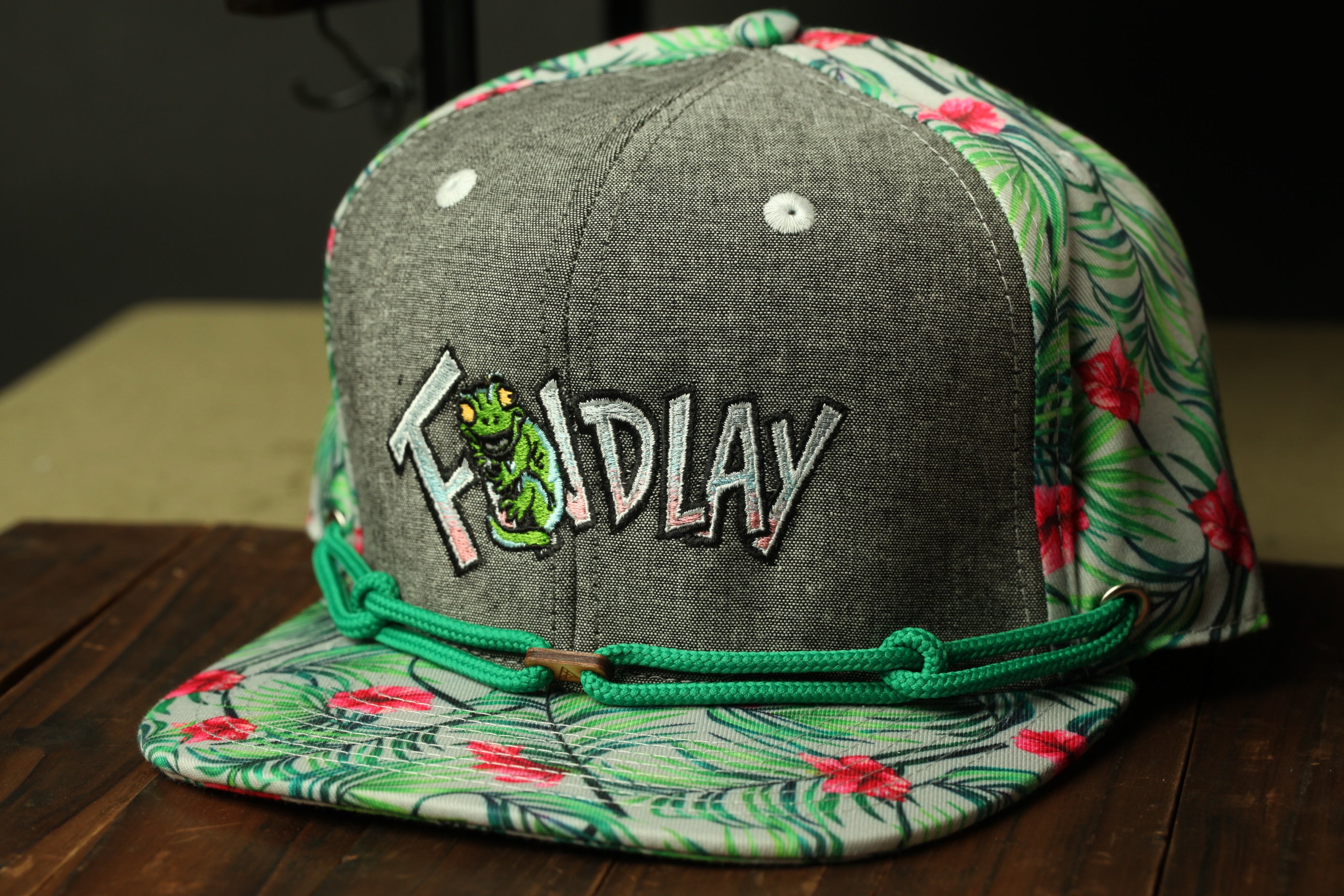 A gray baseball cap with a floral pattern and the word "Foldlay" embroidered on it, sitting on a wooden surface.