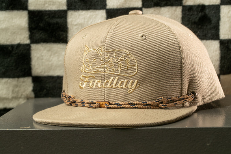 A beige baseball cap with a cat embroidered on it, sitting on a gray surface against a black and white checkered background.