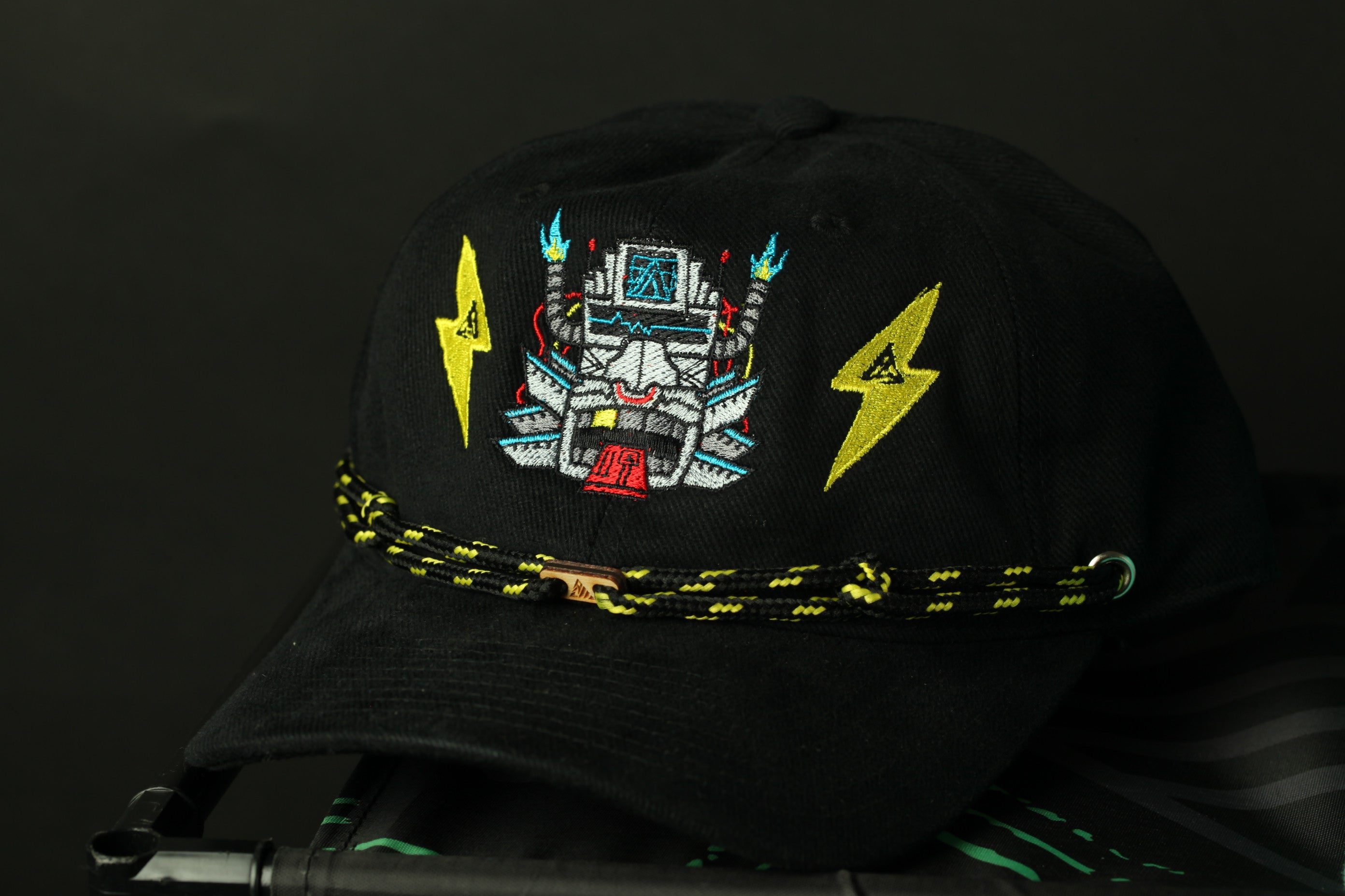 A black baseball cap with a colorful, embroidered design on the front, including a robot-like figure and lightning bolts.