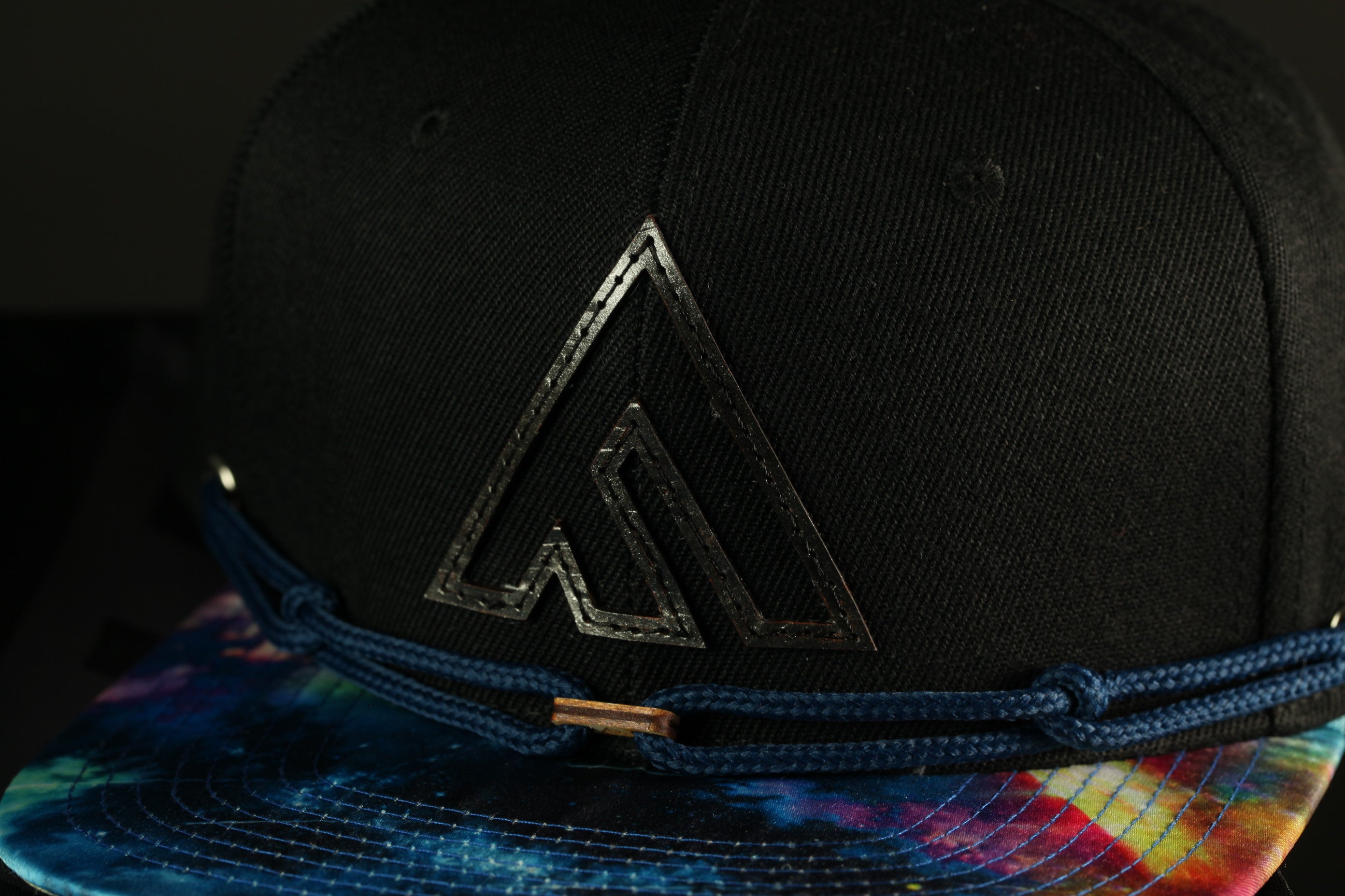 A black baseball cap with a tie-dye pattern and a logo on the front.