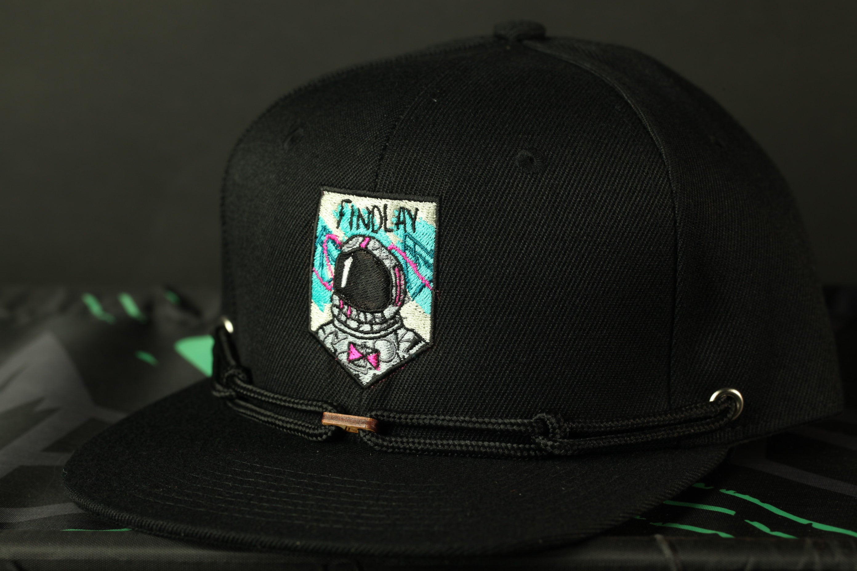 A black baseball cap with a colorful patch featuring an astronaut's helmet and the word "FINDLAY" printed on it.