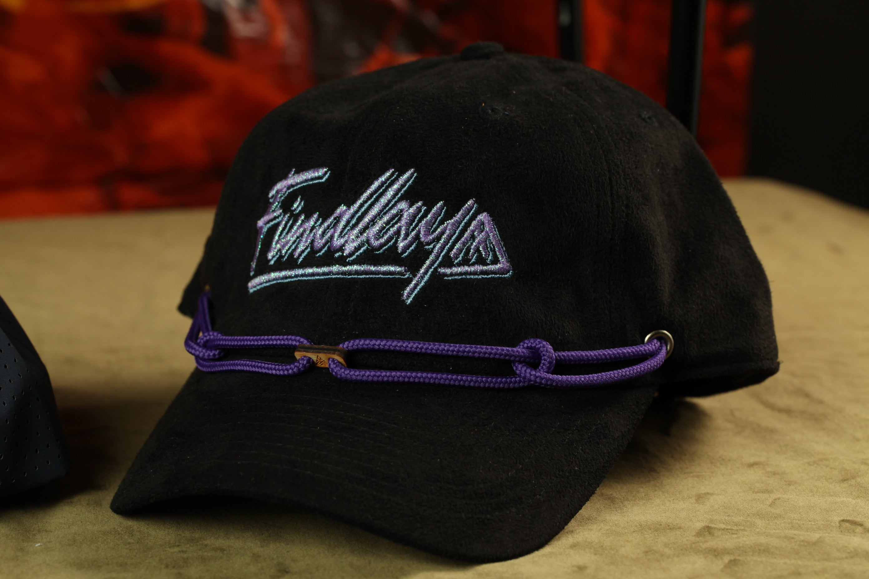 A black baseball cap with purple strings and the word "Findlay" embroidered on it.
