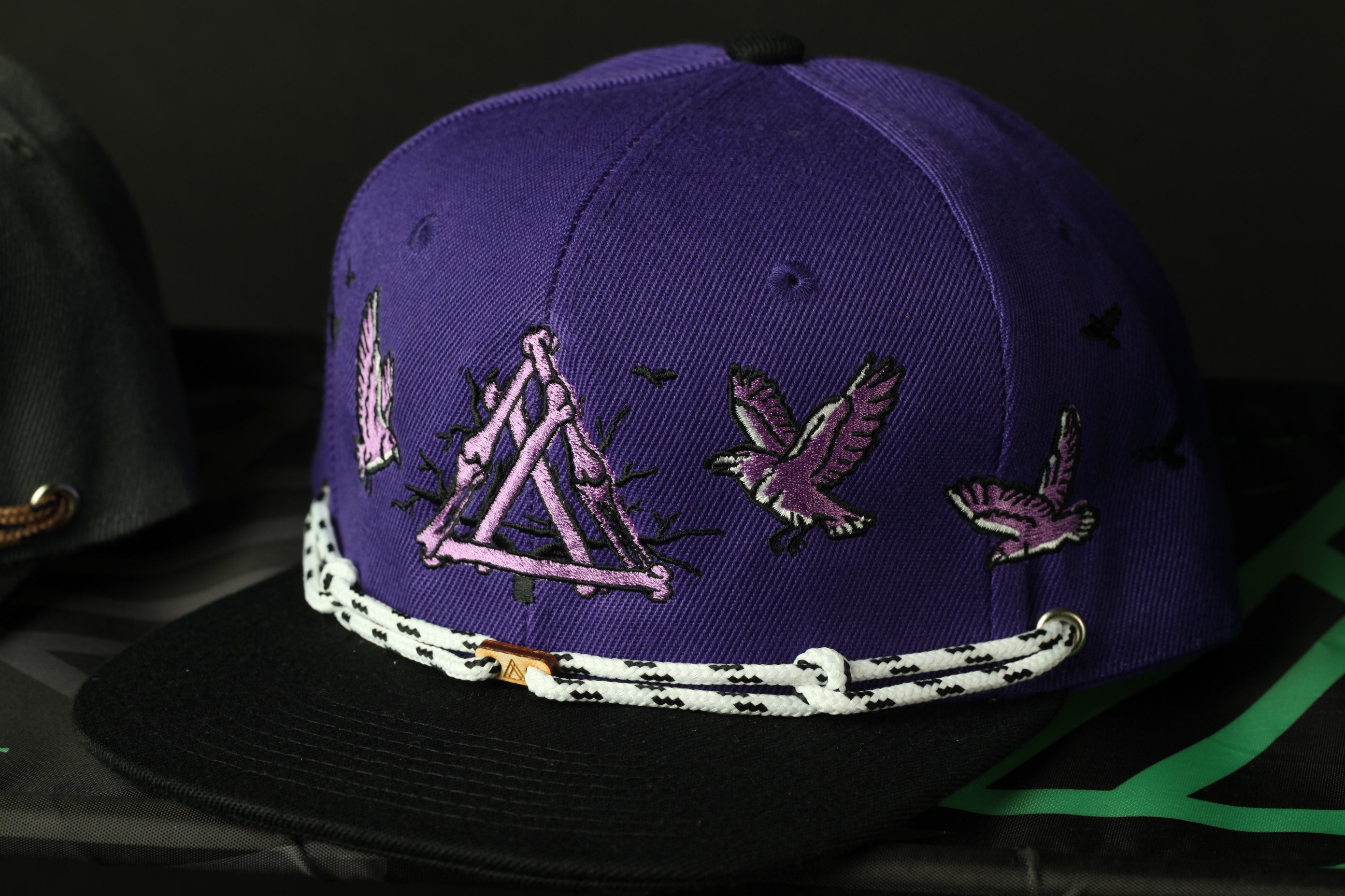 A purple baseball cap with a black brim and white and black patterned string.