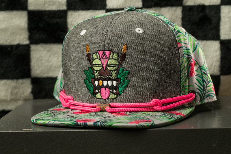 A gray baseball cap with a colorful, cartoonish design on the front, featuring a tiki mask and palm leaves.