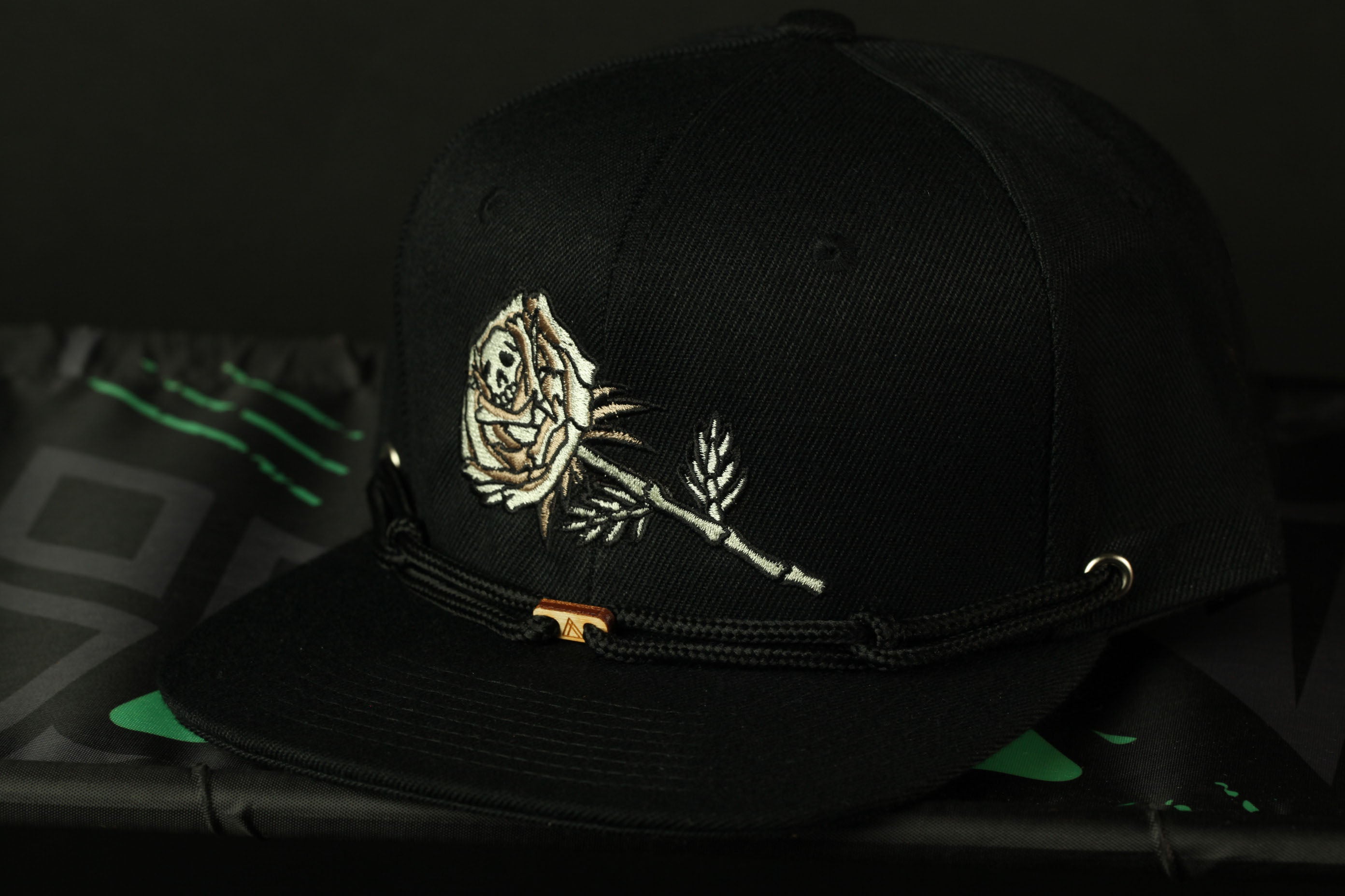 A black baseball cap with a white rose embroidered on the front, resting on a black surface.