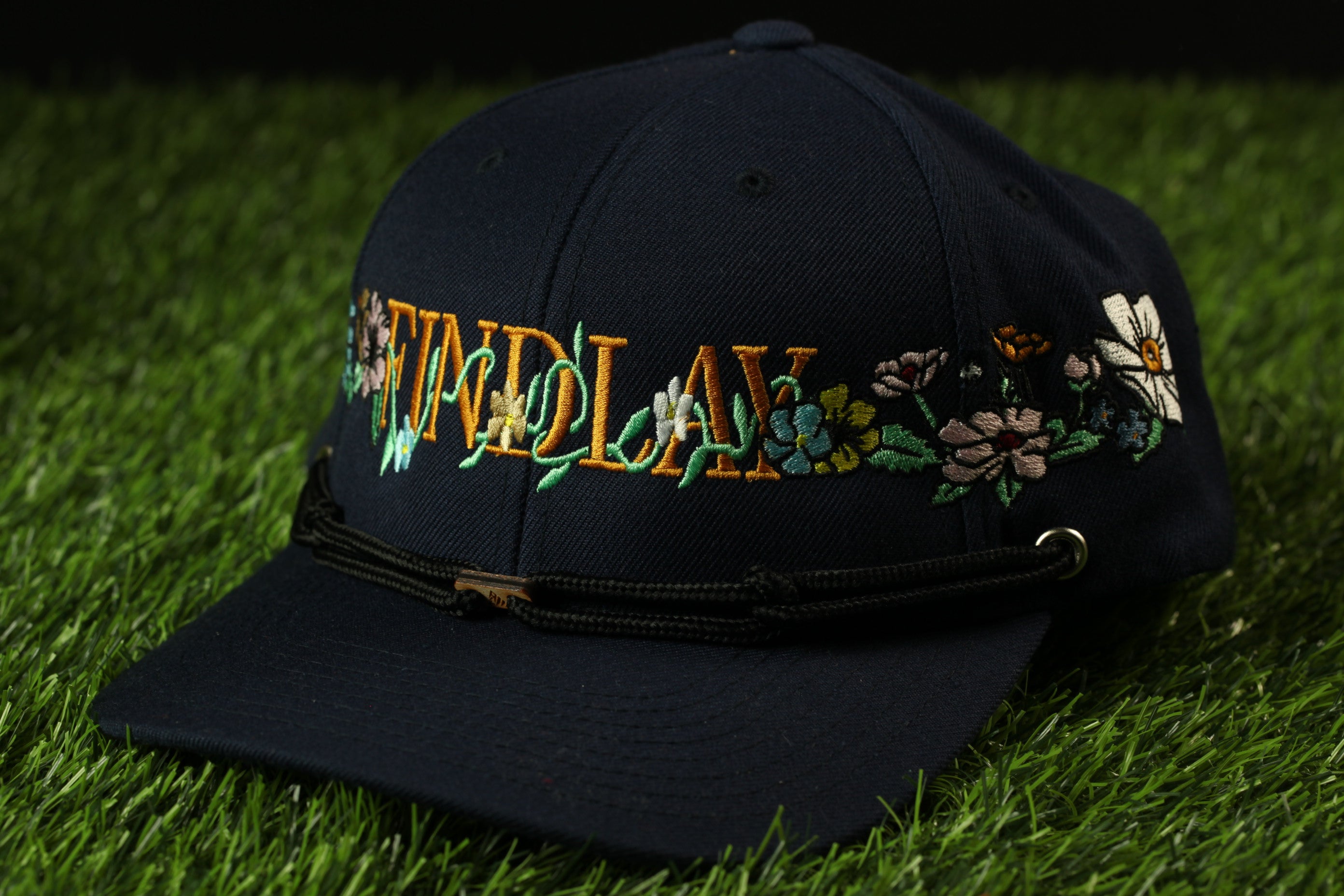A navy blue baseball cap with the word "FIND" embroidered on it, sitting on a grassy surface.
