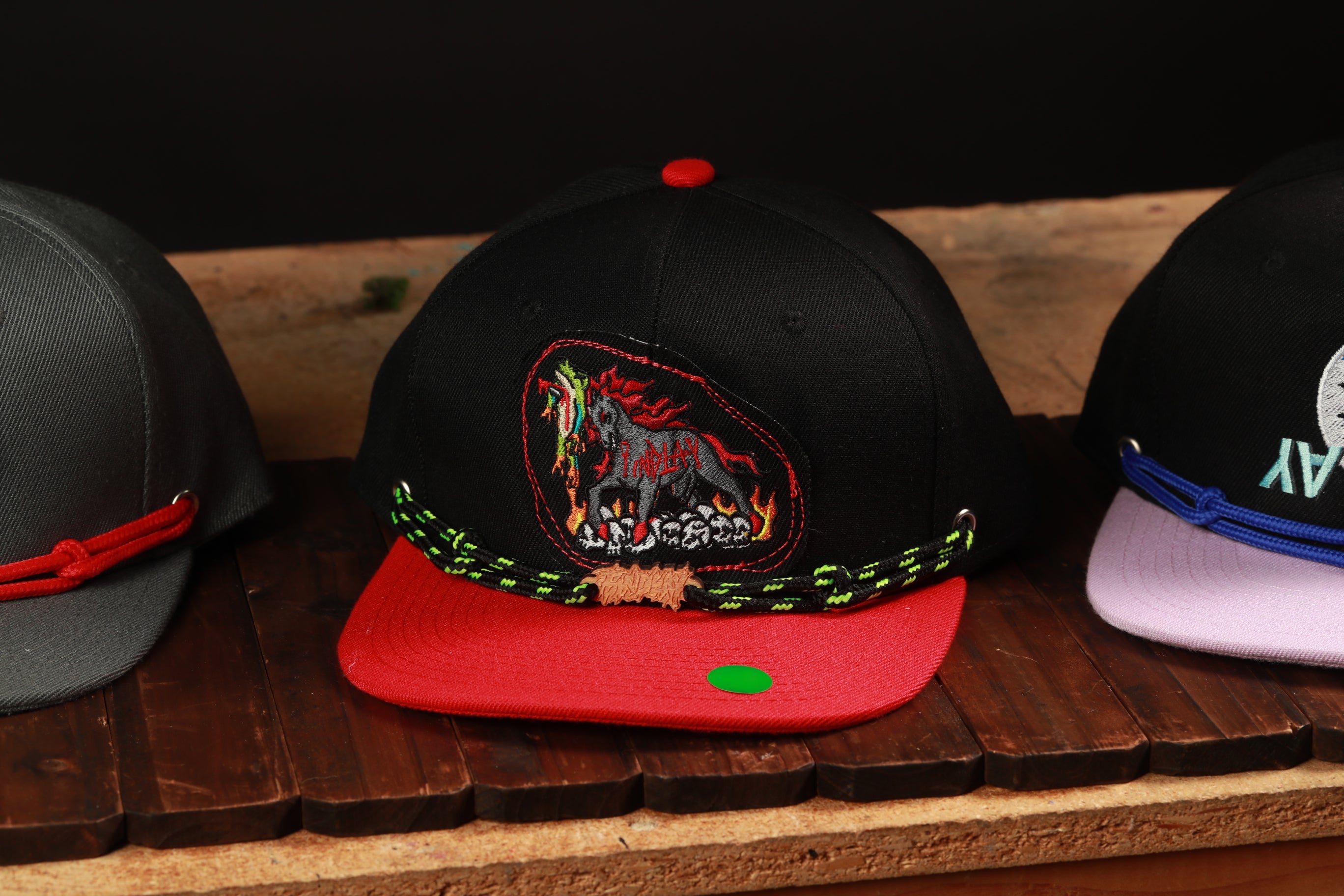 A collection of colorful baseball caps with various designs, including a black cap with a red and green design, a black cap with a white design, and a black cap with a white design.