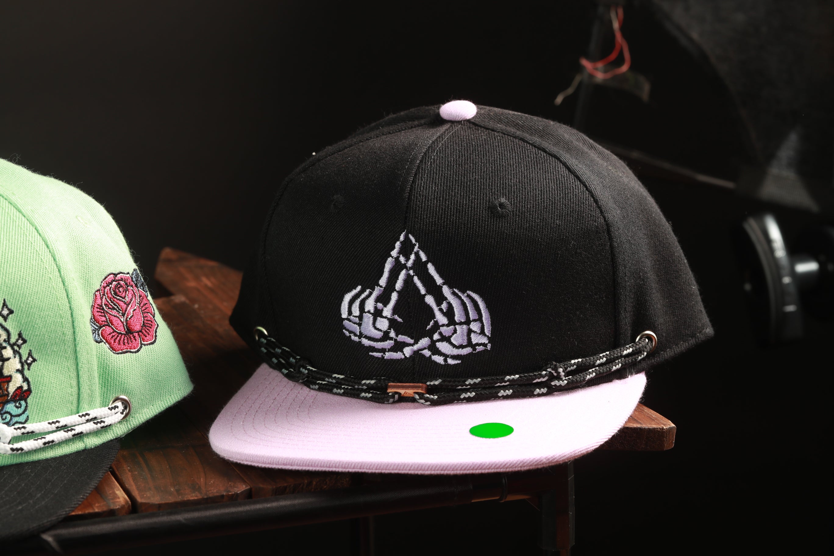 a black baseball cap with a white skull and crossbones design, placed on a wooden surface.