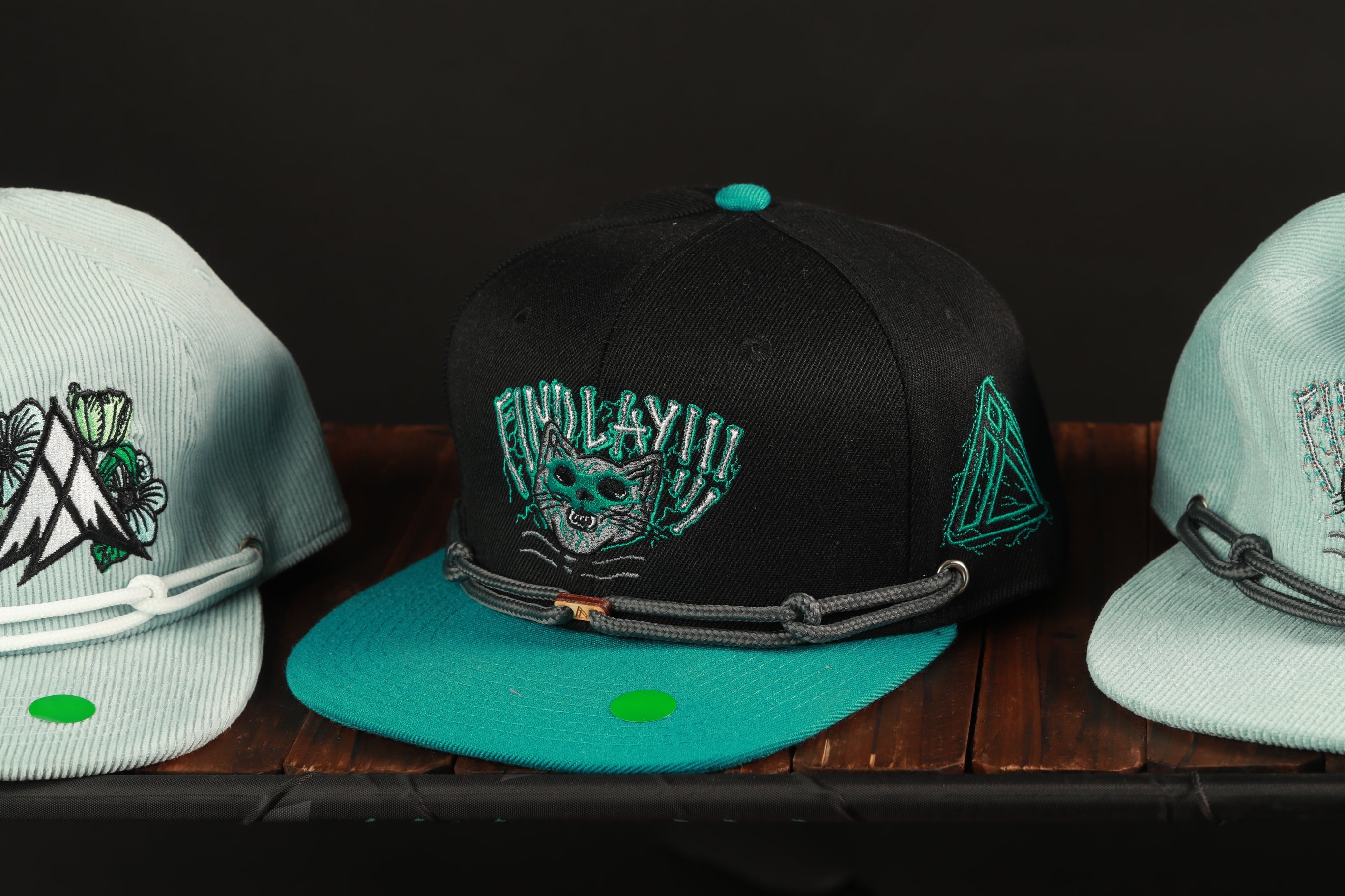 Three baseball caps are displayed on a wooden surface, each with unique designs and colors.