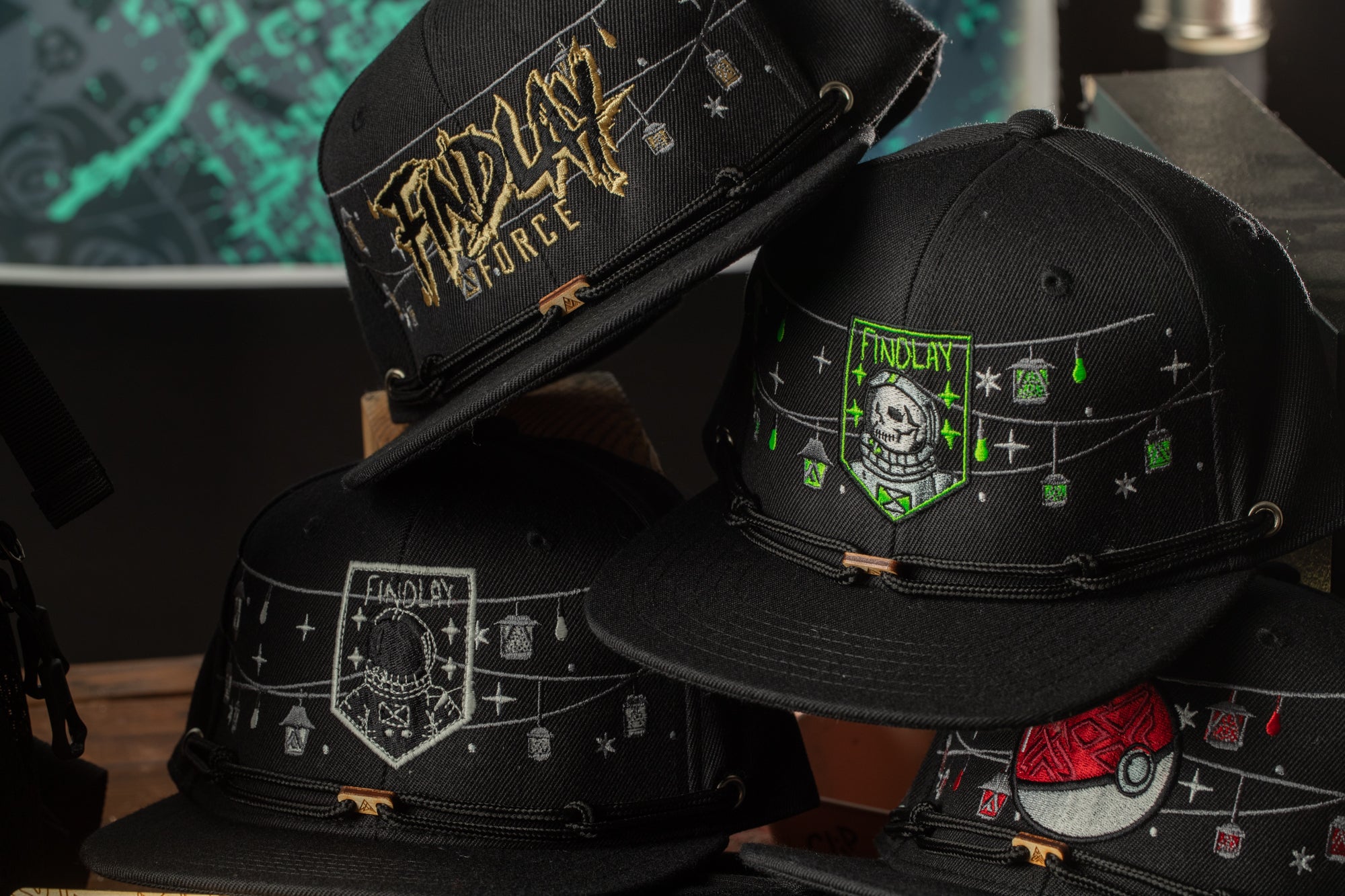 A collection of black baseball caps with various designs and text, including a skull and crossbones motif, a "Findlay" logo, and other decorative elements.