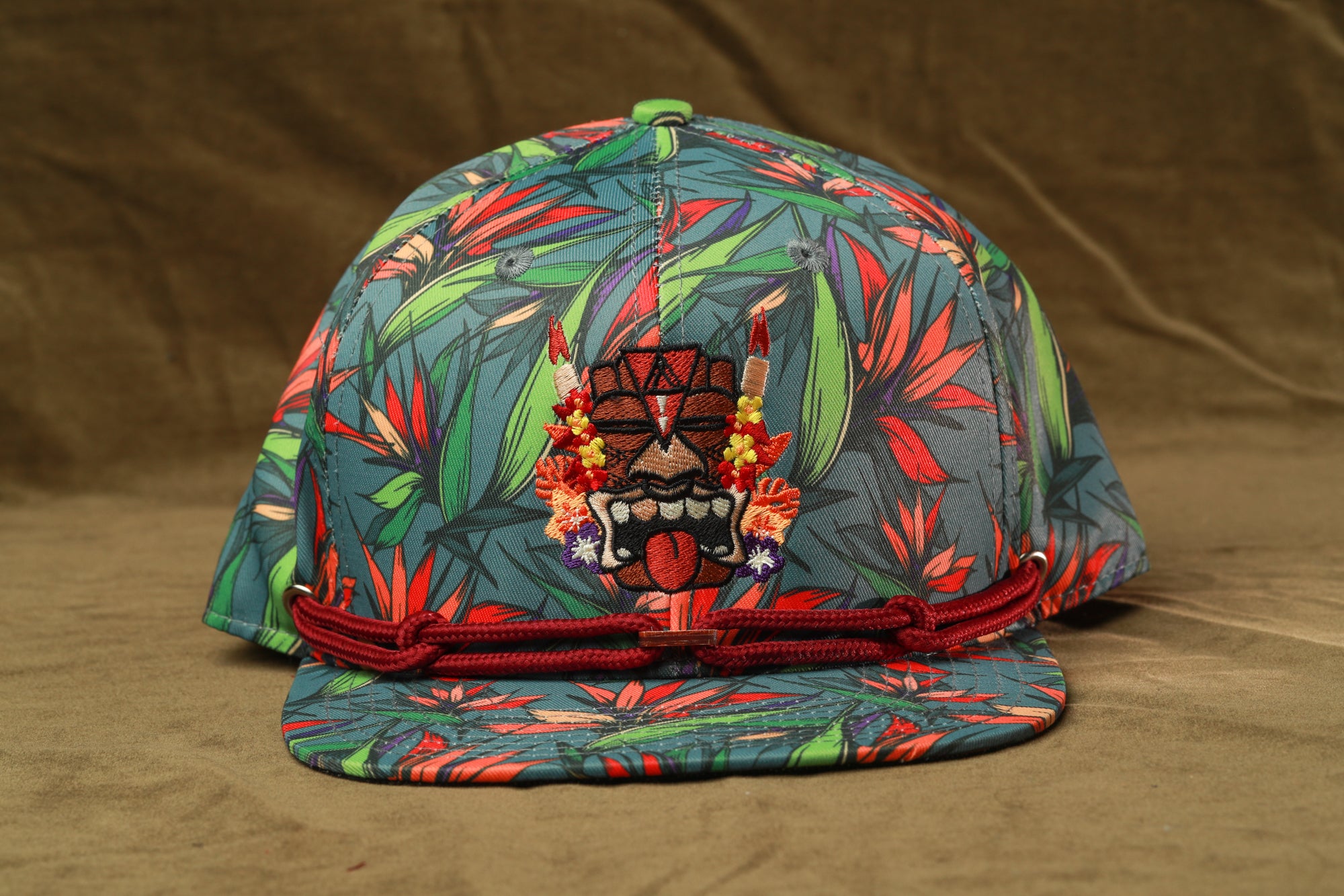 A colorful floral-patterned baseball cap with a decorative tiki mask design on the front.