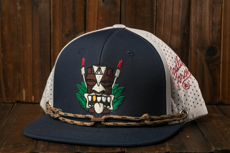 A navy blue baseball cap with a white and red tiki mask design on the front, sitting on a wooden surface.