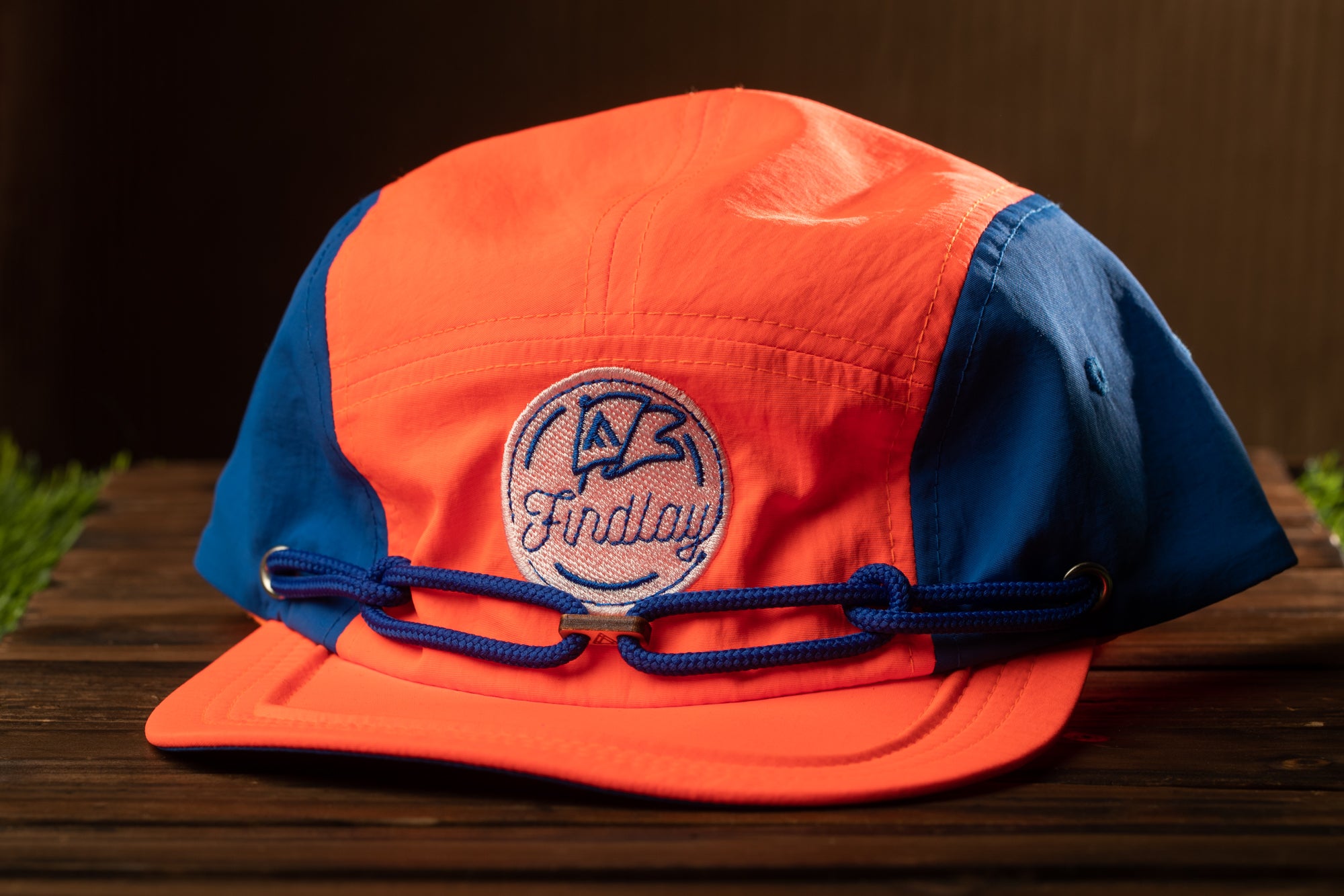 An orange and blue baseball cap with a blue logo on the front, resting on a wooden surface.