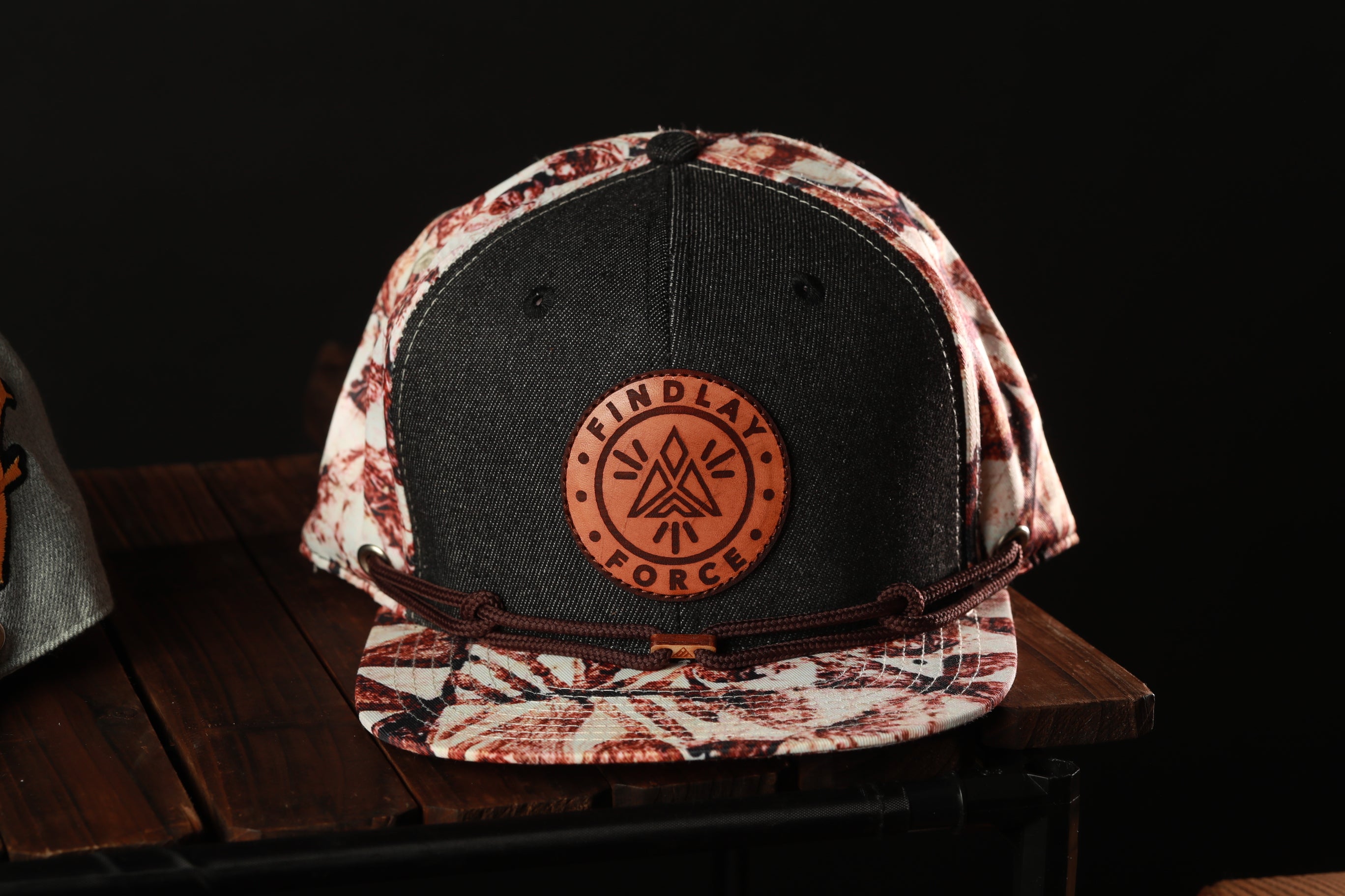 A black and white patterned baseball cap with a circular logo on the front, sitting on a wooden surface.