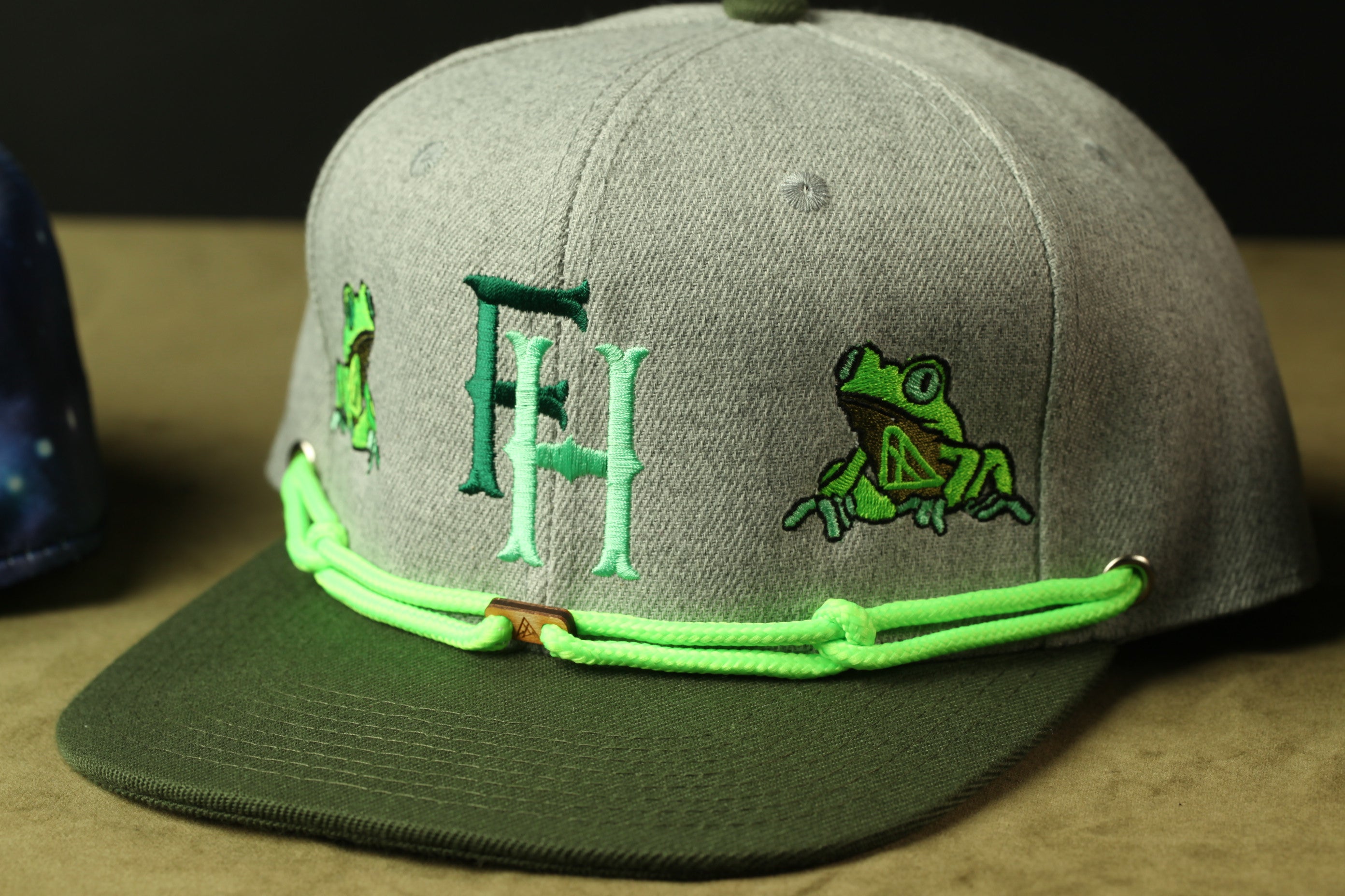 A gray baseball cap with green embroidered characters and a frog design.