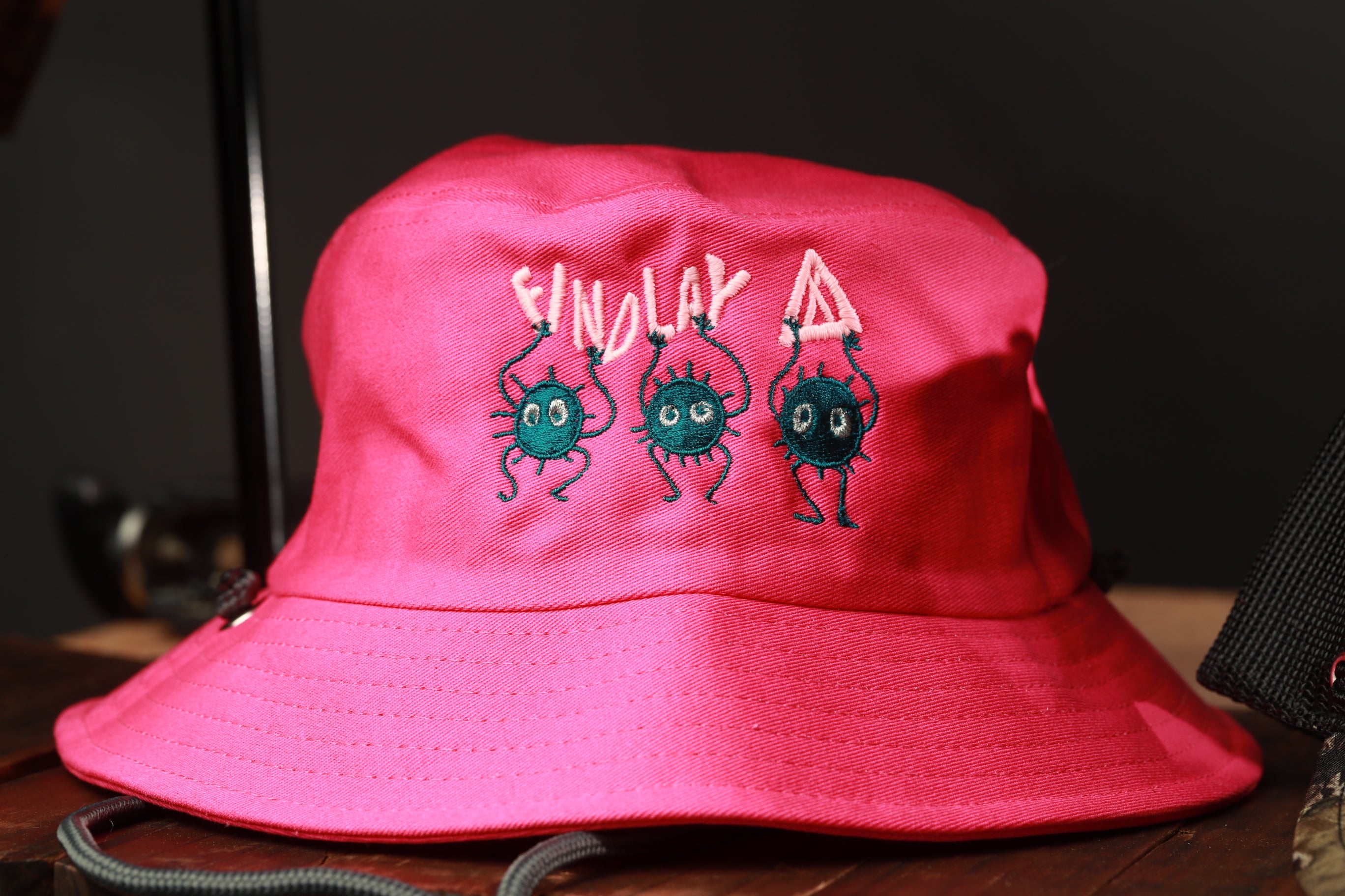 A bright pink bucket hat with a cartoon character design and text on it.