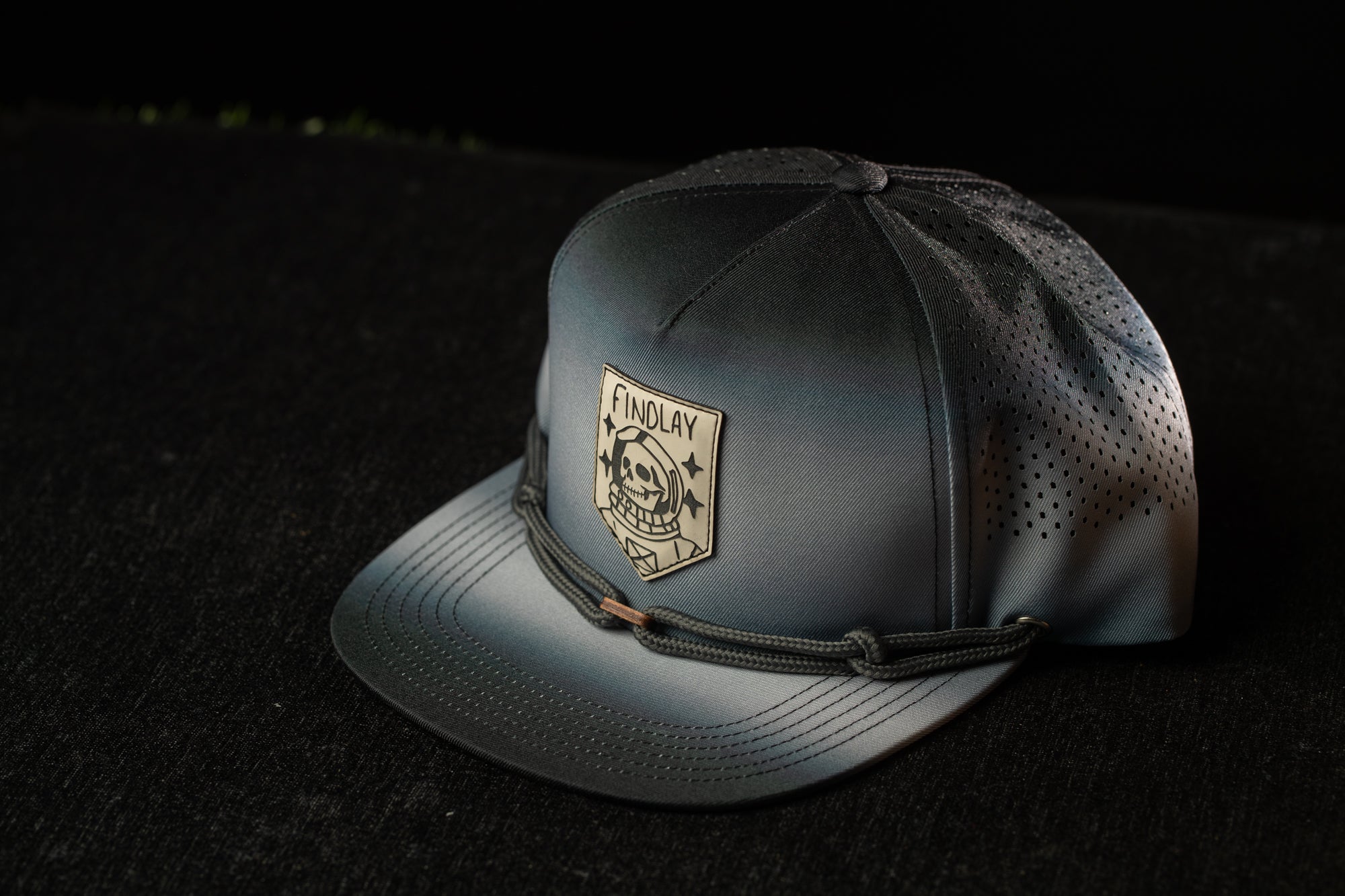 A black and gray baseball cap with a logo on the front, placed on a dark surface.