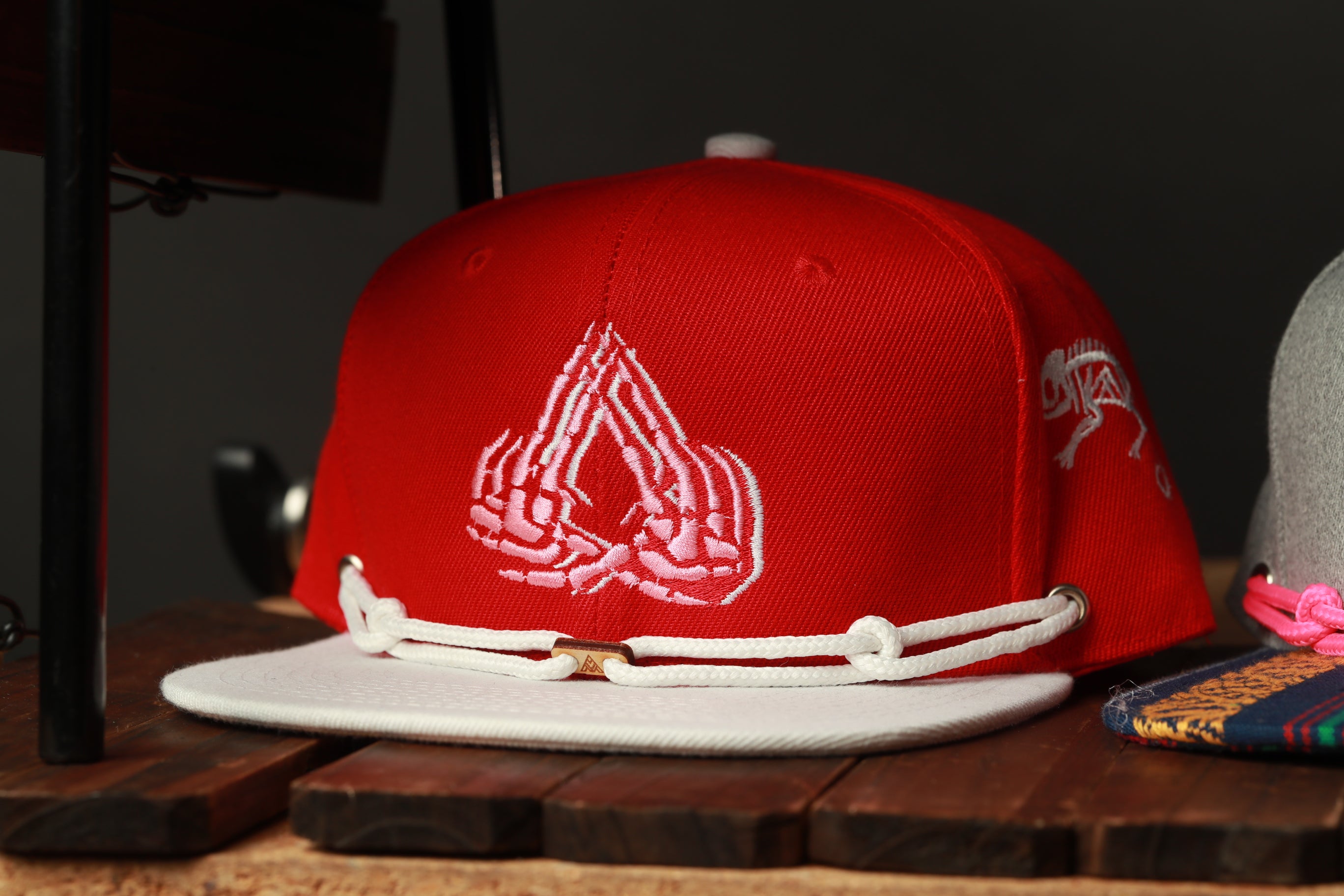 A red baseball cap with a white band and a white logo on the front, placed on a wooden surface.
