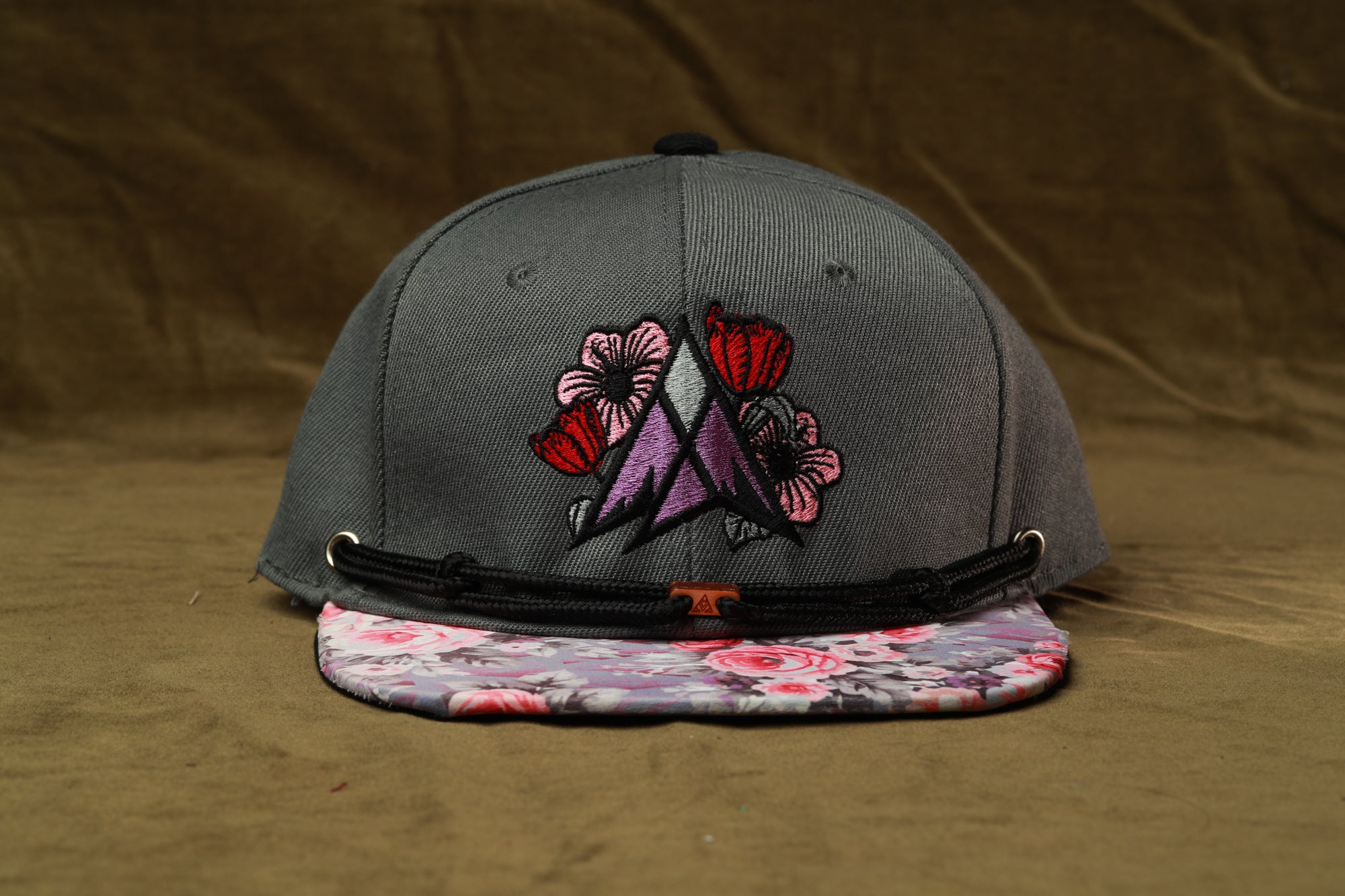 A gray baseball cap with a floral pattern on the front and a black strap.