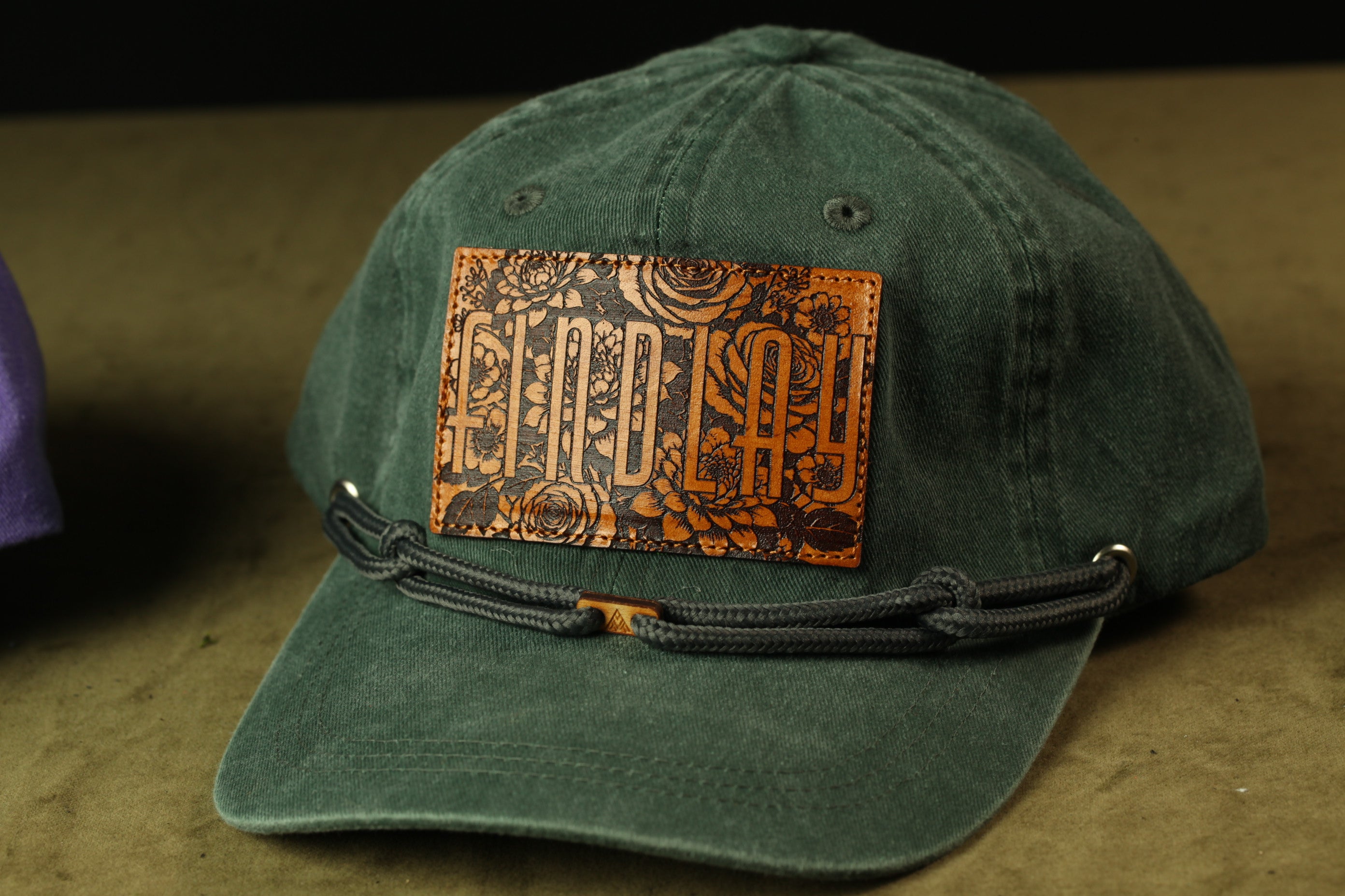A green baseball cap with a leather patch on the front displaying the word "SUNDAY".