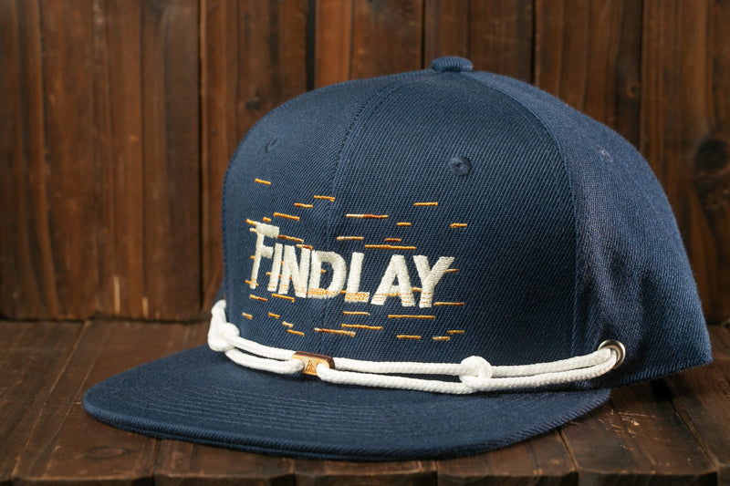 A navy blue baseball cap with the word "FINDlay" printed on it, sitting on a wooden surface.
