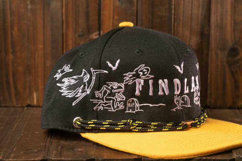 A black baseball cap with a yellow brim, featuring embroidered designs and text on the front.