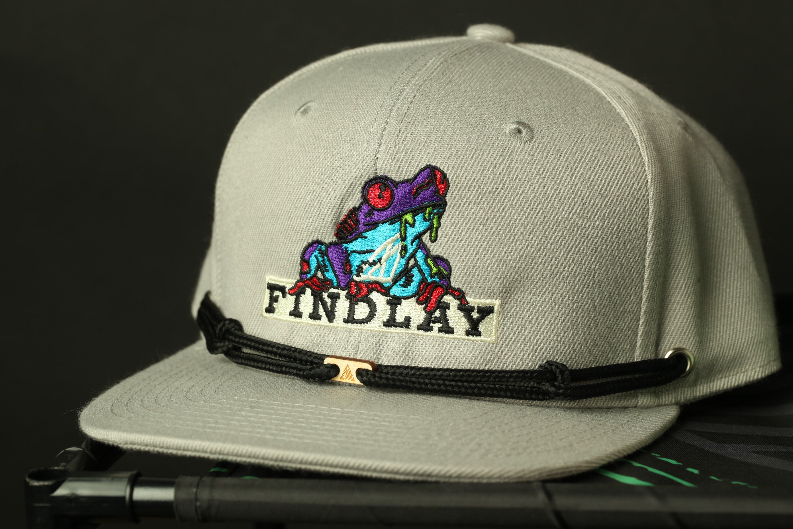 A gray baseball cap with a colorful frog embroidered on it, and the word "FINDLAY" printed on it.