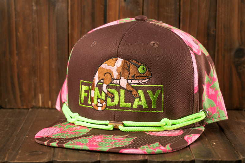 A brown baseball cap with a floral pattern and a chameleon design, featuring the word "FINSLAY" in green text.