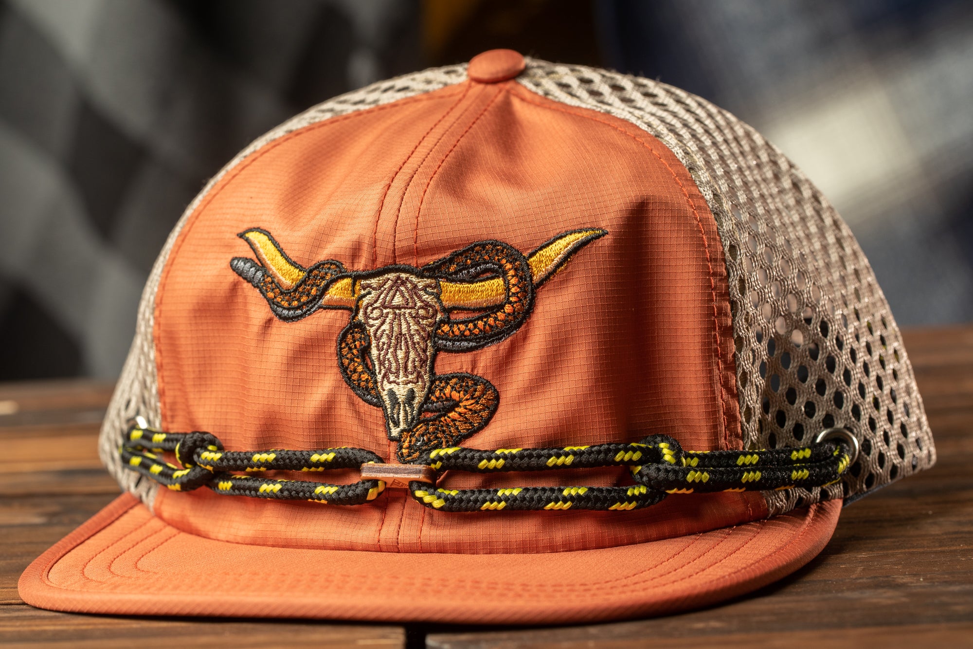 An orange baseball cap with a mesh back and a black and yellow chain strap.
