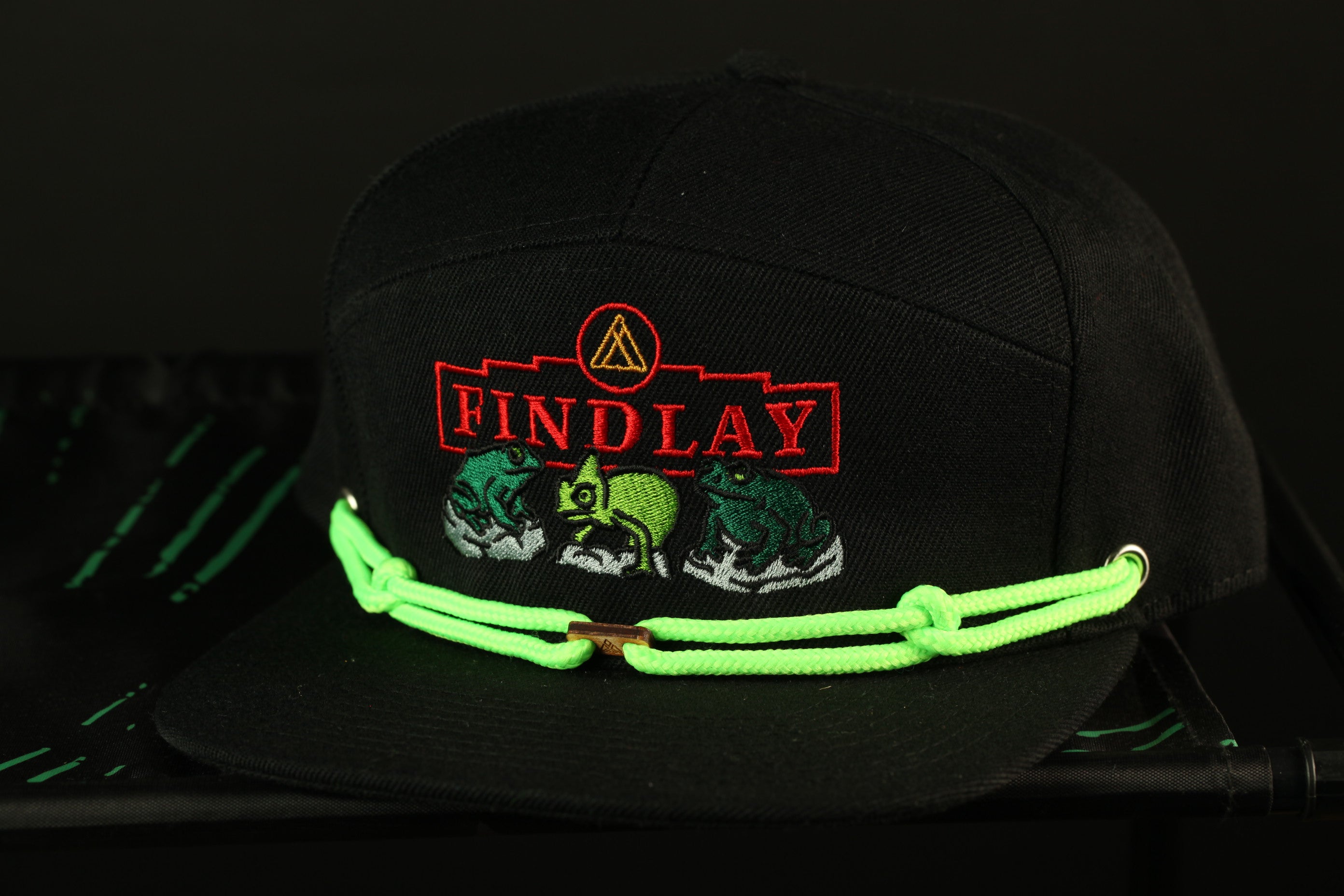 A black baseball cap with a neon green string and a red and white logo on the front.