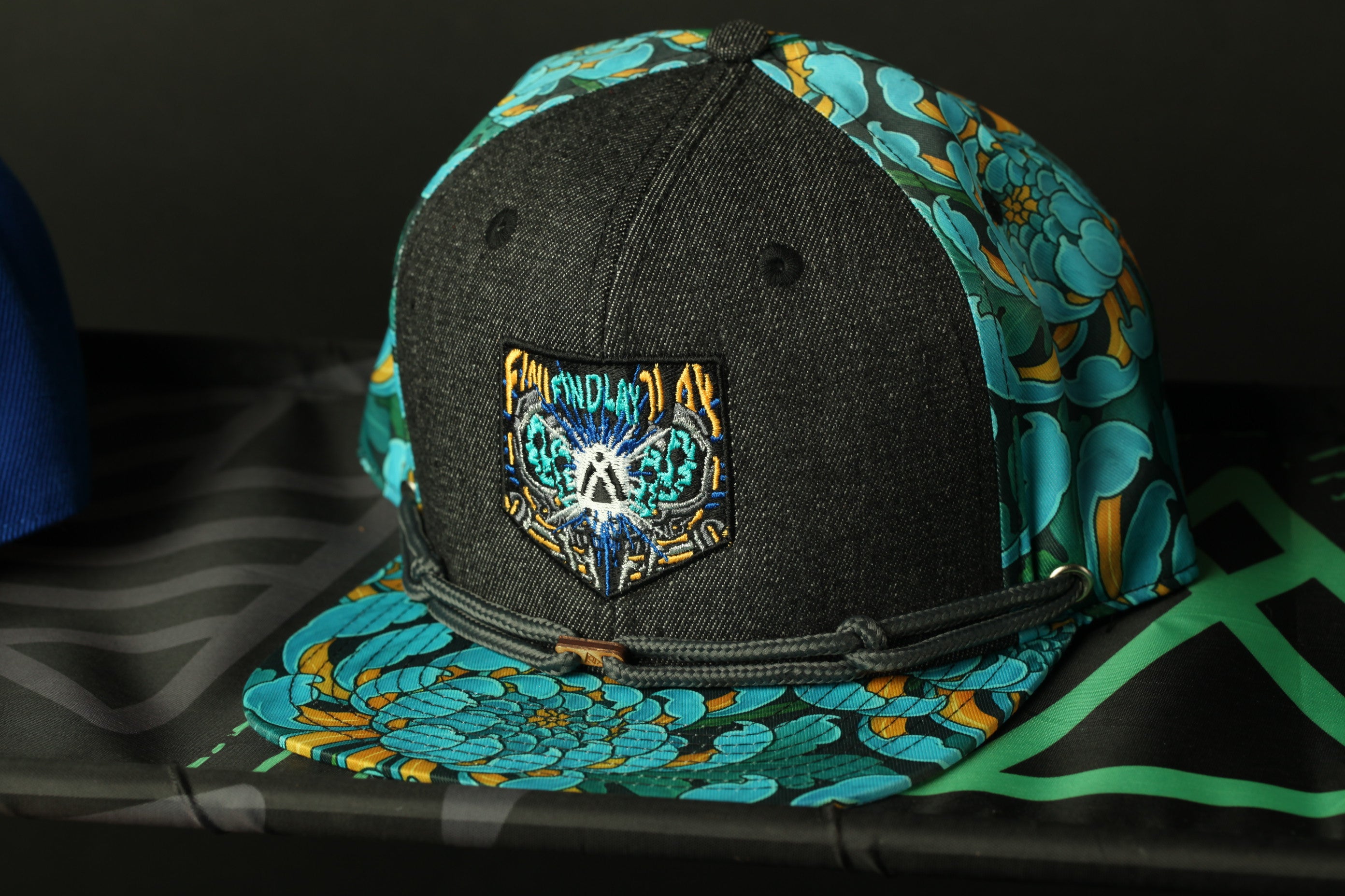 A black baseball cap with a colorful floral pattern and a patch on the front, placed on a black surface.