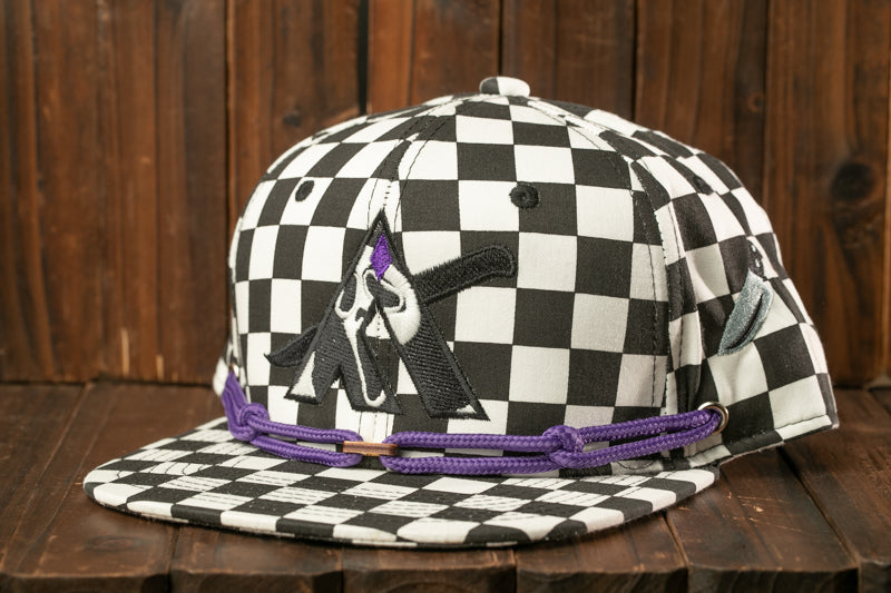 A black and white checkered baseball cap with a purple embroidered logo on the front, sitting on a wooden surface.