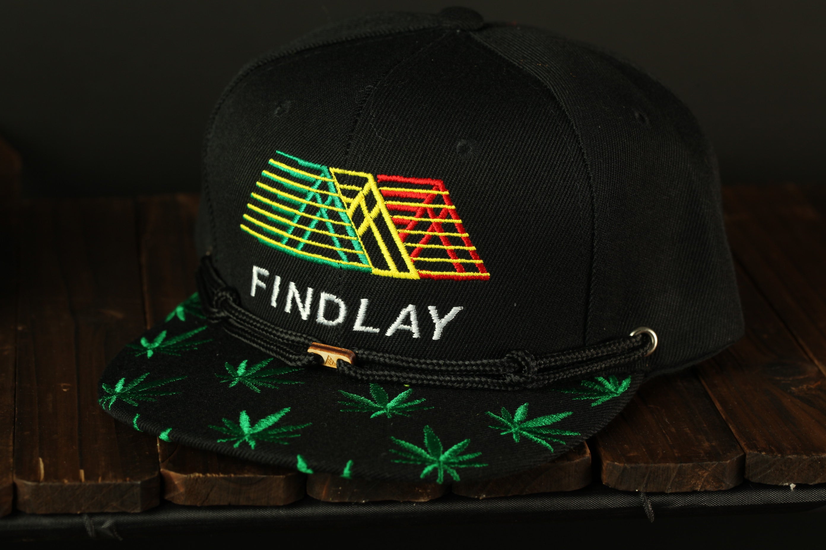 A black baseball cap with a colorful geometric design and the word "FINDLAY" printed on it, sitting on a wooden surface.